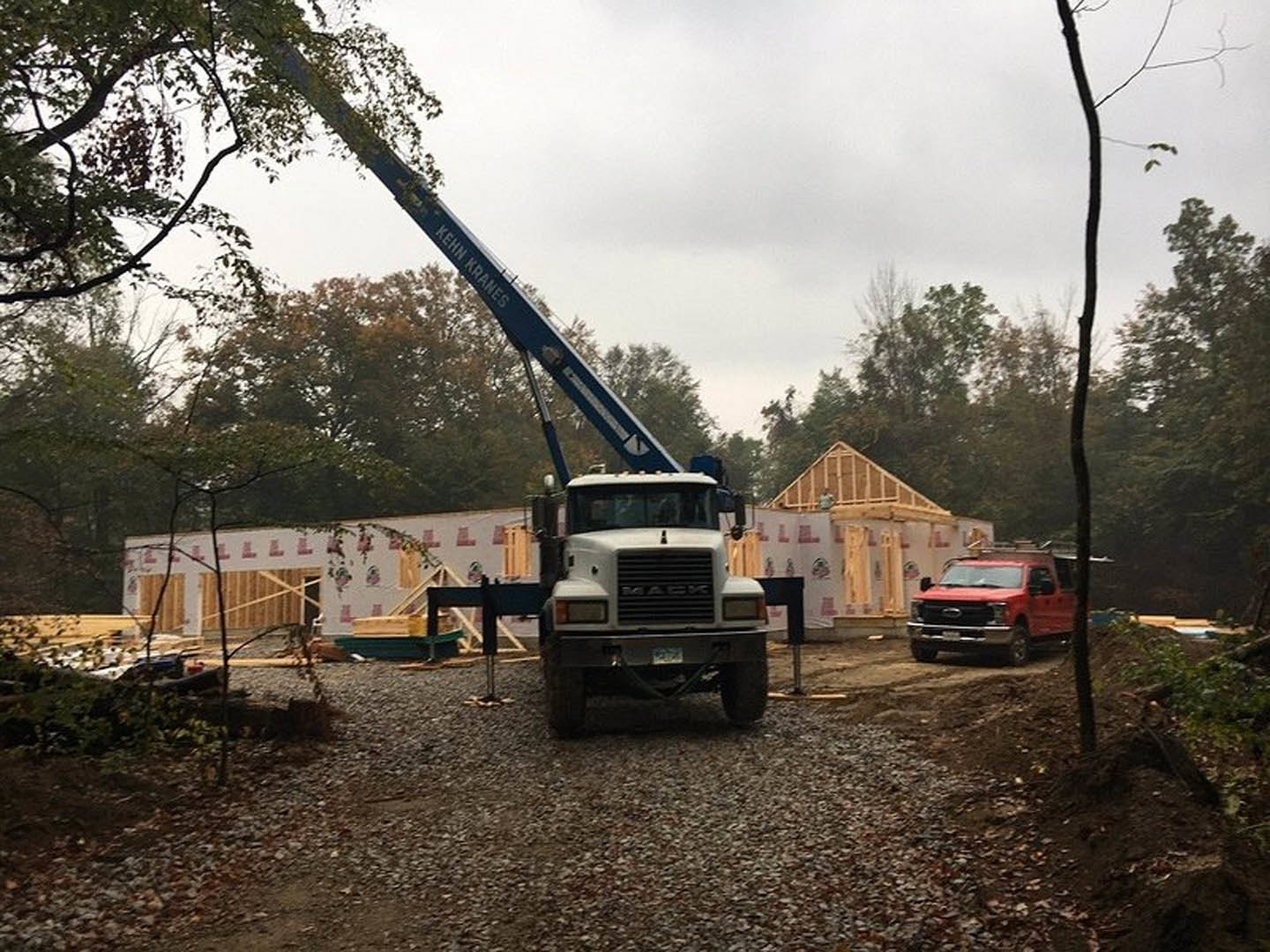 Red construction truck with crane parked on dirt driveway beside trees under cloudy sky