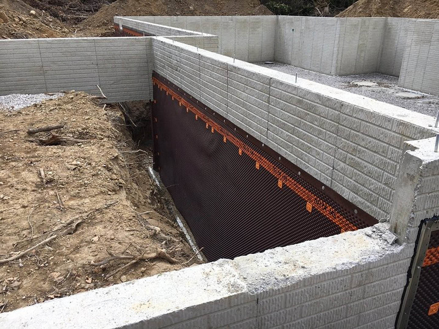 Concrete foundation with metal framing set into excavated ground, surrounded by soil and unfinished cement walls