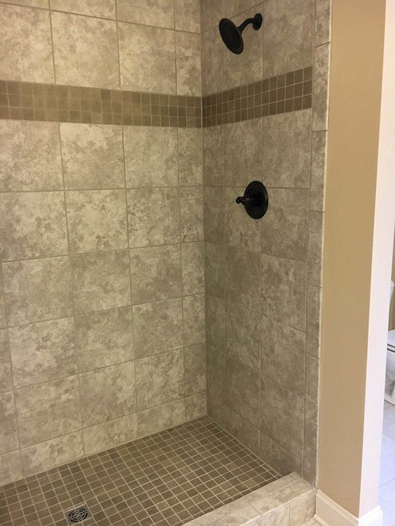 Shower with marble tile walls, black shower head, close-up of tile floor and chrome knob
