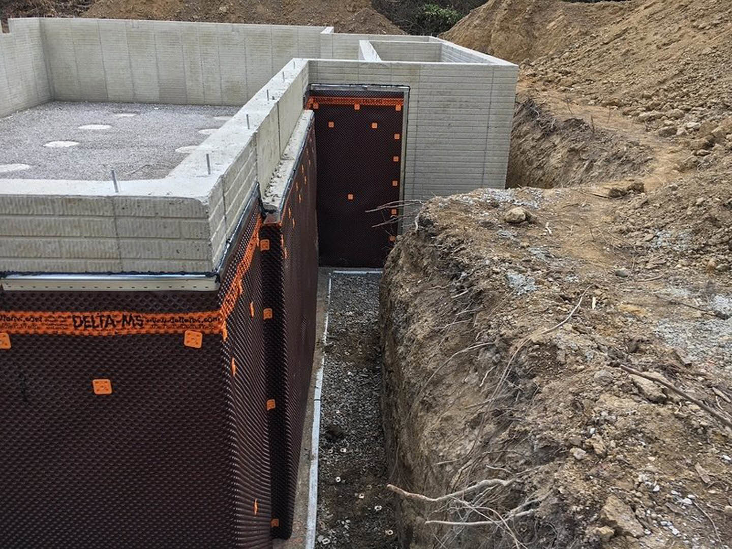 Concrete foundation with exposed metal rebar set on a dirt construction site, surrounded by soil and sparse vegetation.