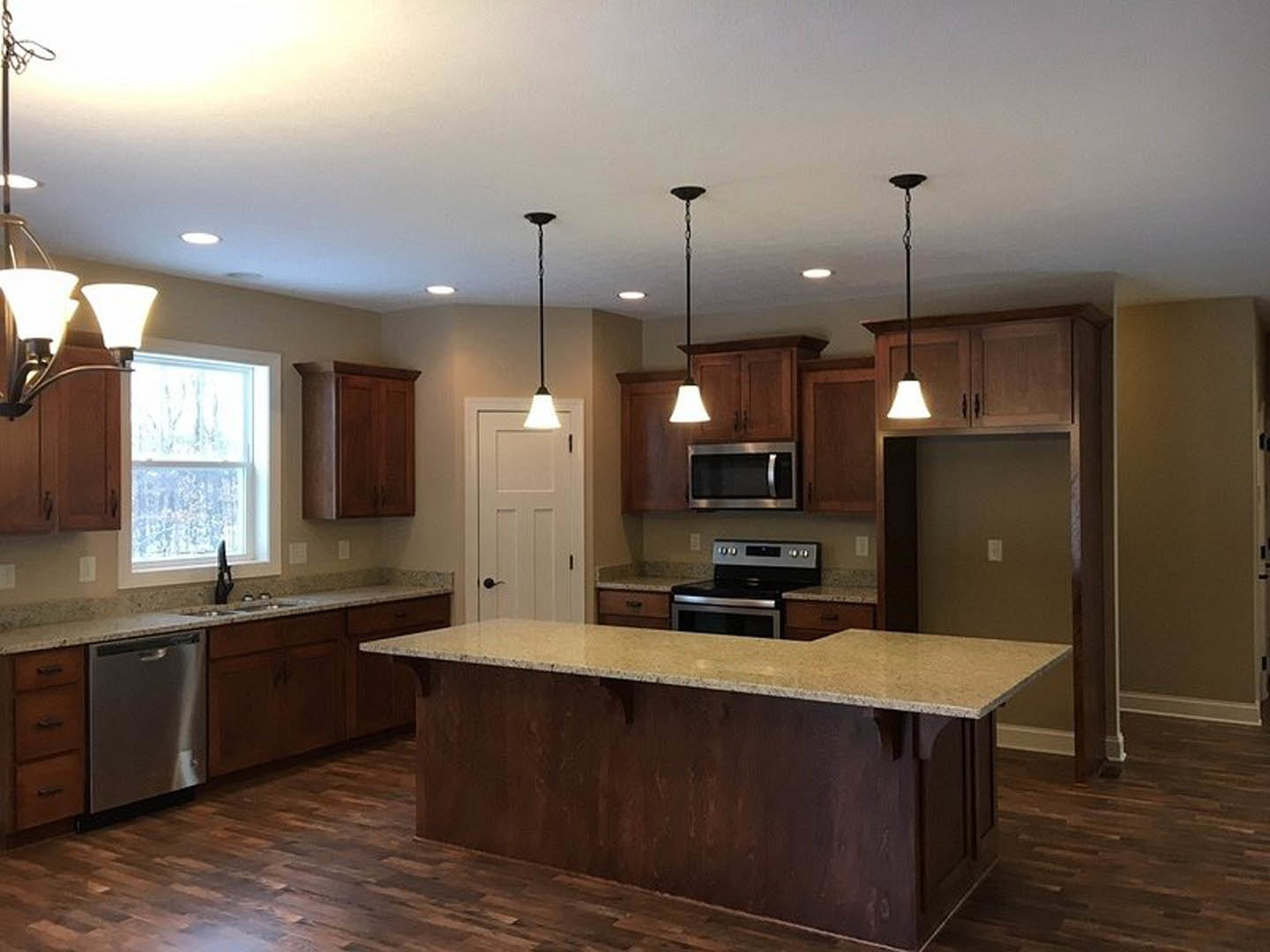 Spacious kitchen featuring a large quartz island, stainless steel stove and microwave, white cabinetry, built-in dishwasher, and window overlooking the outdoors