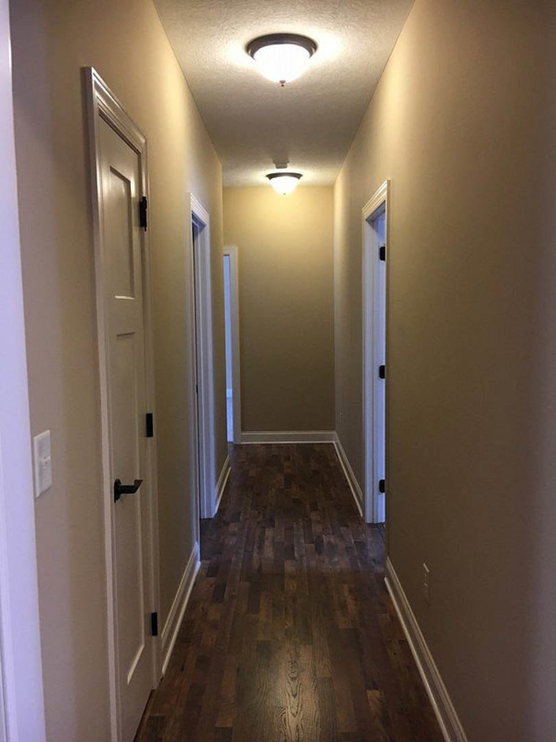 Hallway with dark wood flooring, white baseboards, white door with black handle, and ceiling light fixture