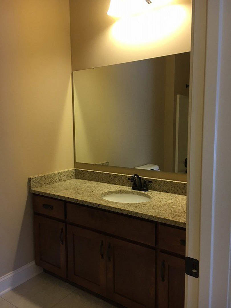 Modern bathroom featuring a round mirror above a white countertop with chrome faucet, light gray tile backsplash, and sleek cabinetry.