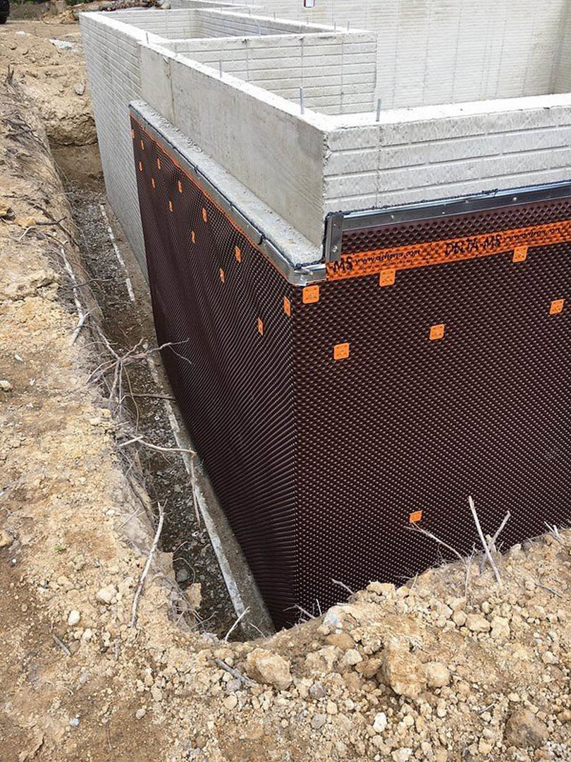 Concrete house foundation with exposed metal rebar, surrounded by gravel and patches of grass