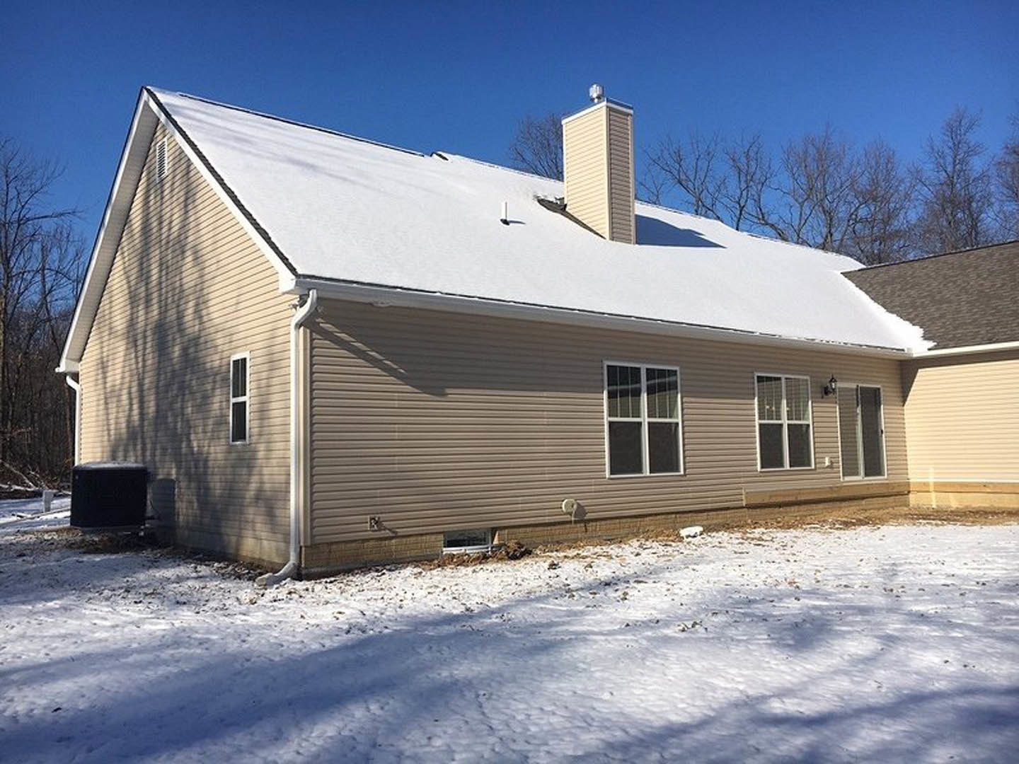 Two-story home with white siding and dark-framed windows, snow covering the roof and ground, bare trees in the yard, overcast winter sky
