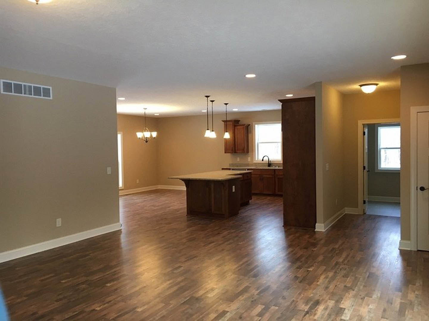 Open-concept kitchen and living room featuring hardwood floors, marble-topped kitchen island, white-framed window, open door, and ceiling light fixture