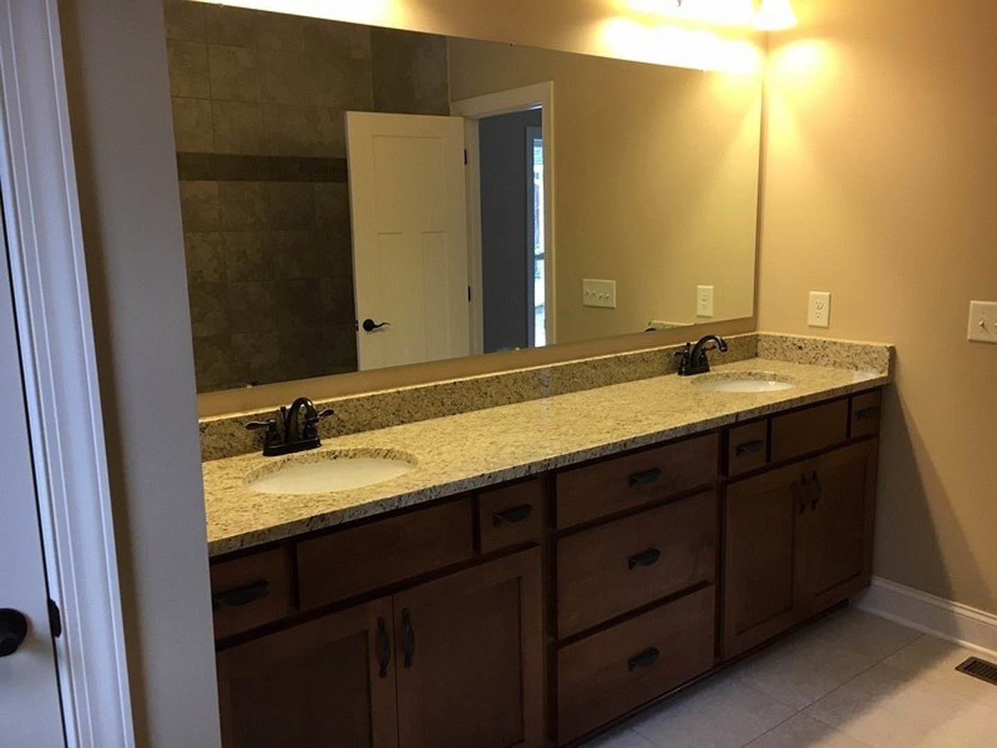 Bathroom with double sinks, marbled countertop, chrome faucets, white cabinetry with black handles, and white tile walls