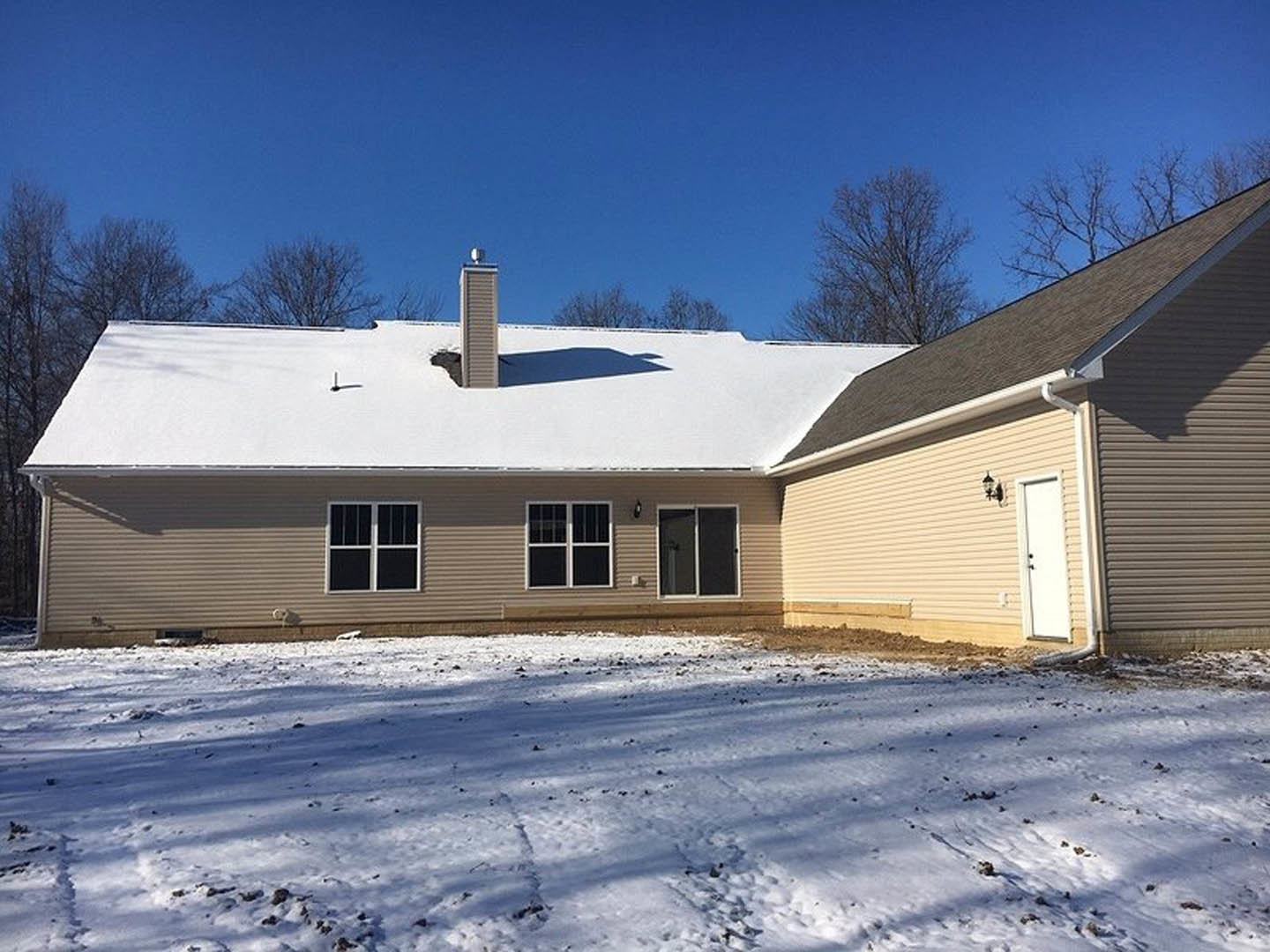 Two-story house with white siding, large windows with white trim, glass-paneled front door, snow covering the ground and roof, winter sky in the background