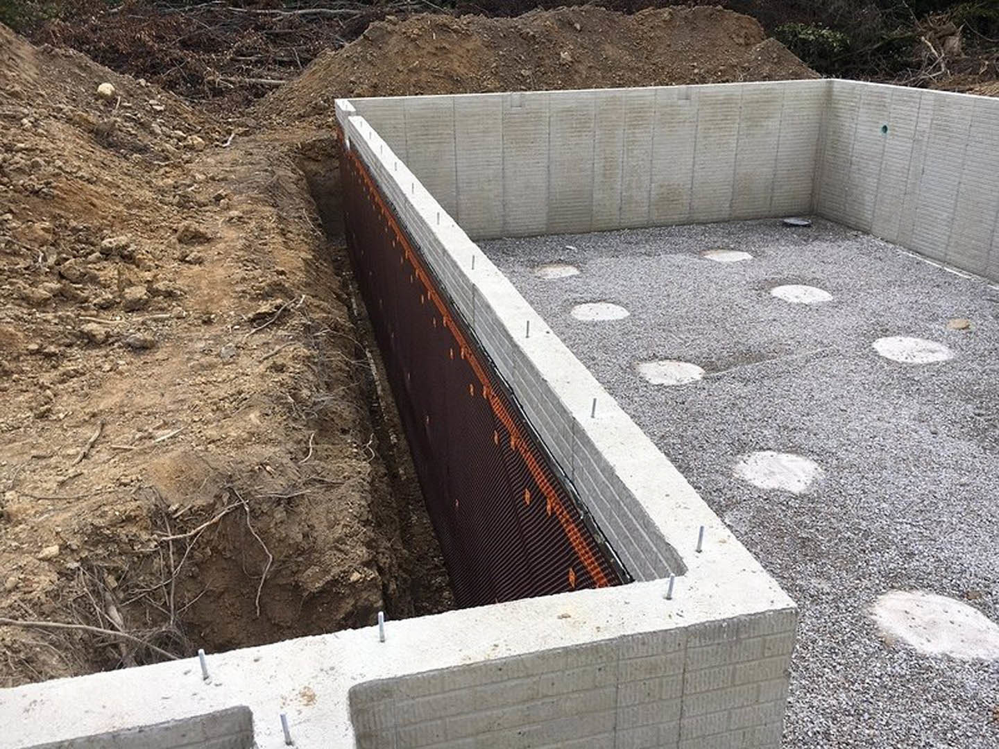 Concrete foundation with black and orange mesh reinforcement, surrounded by soil and dirt, metal retaining wall, white construction material on ground