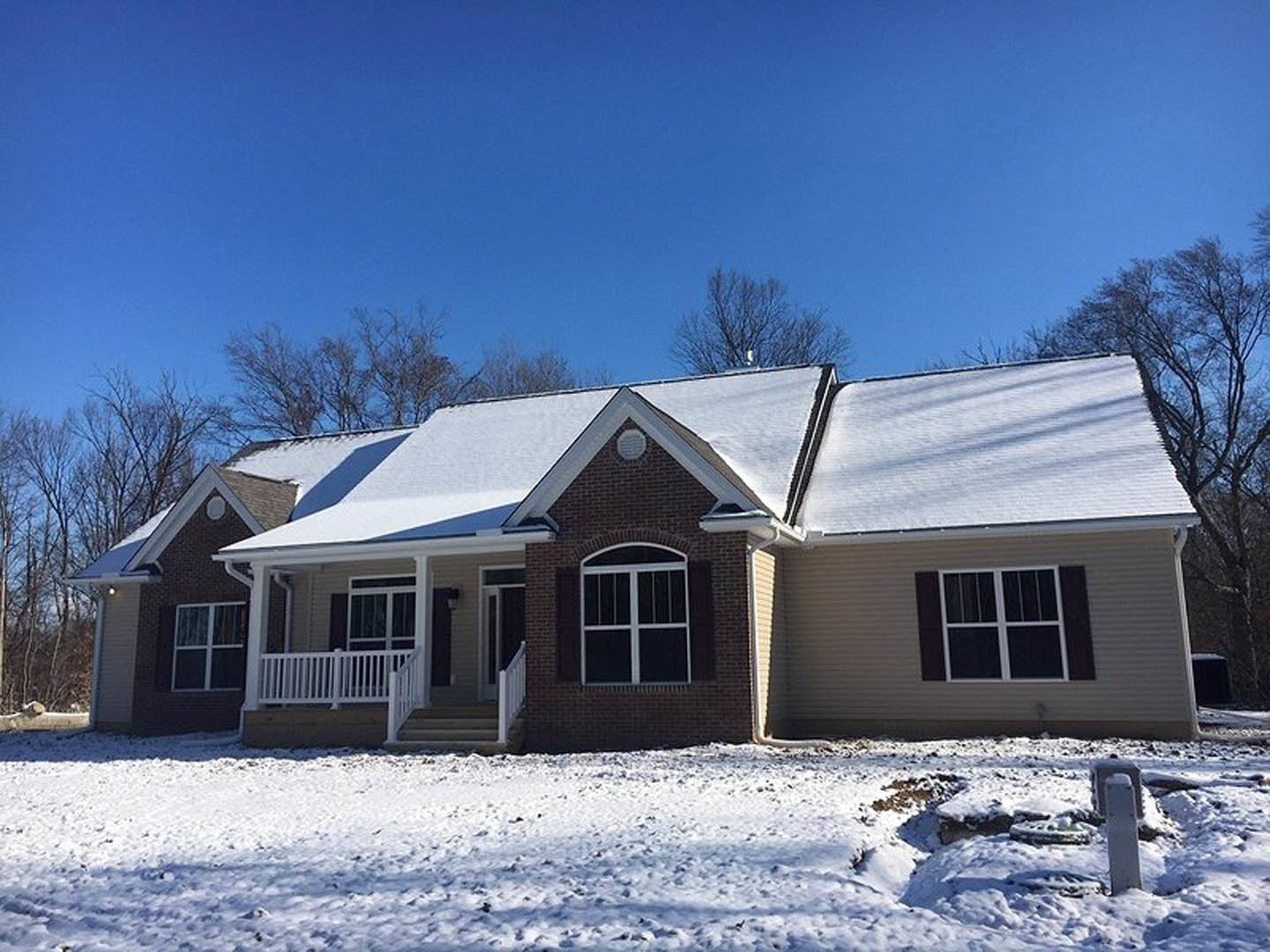Two-story house with white siding, snow-covered roof and ground, white porch railing, footprints in snow, white-framed windows, leafless trees in background