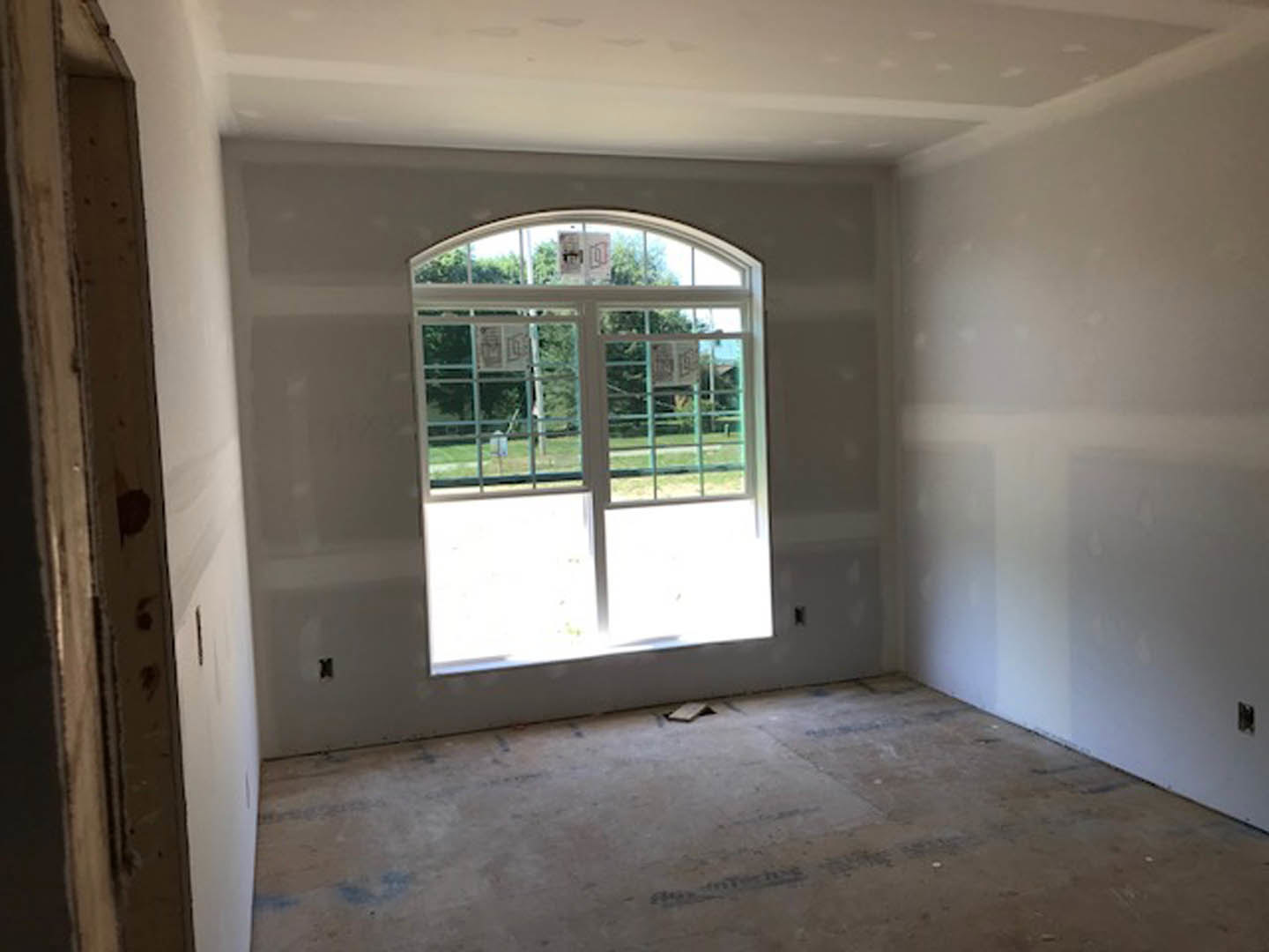Concrete floor with smooth finish, large window framed in wood, white plaster walls, natural daylight illuminating minimalist interior
