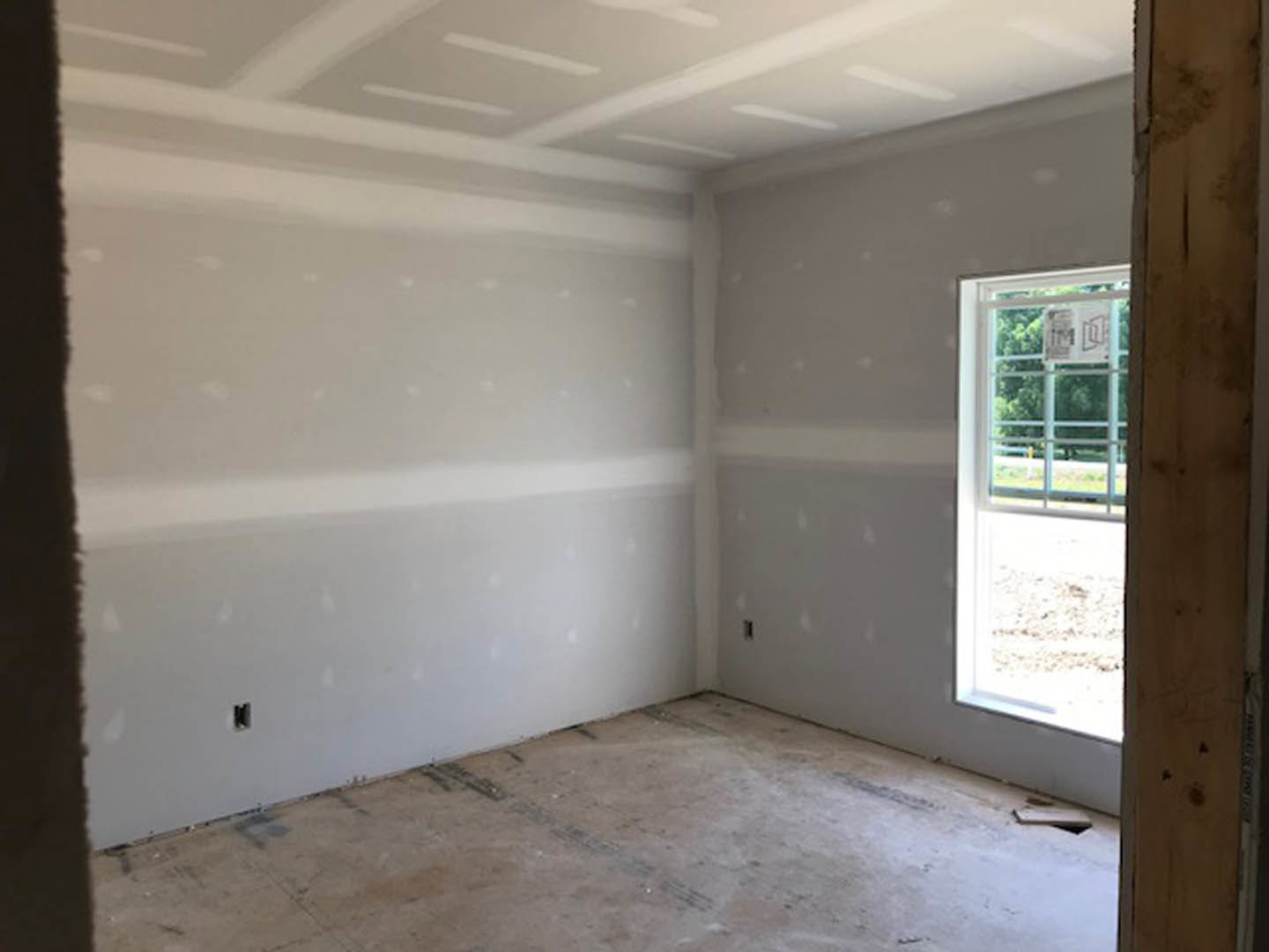 Bright room featuring two large windows, white plaster walls, wood flooring, and a white ceiling with linear detailing; view of a metal fence outside one window.
