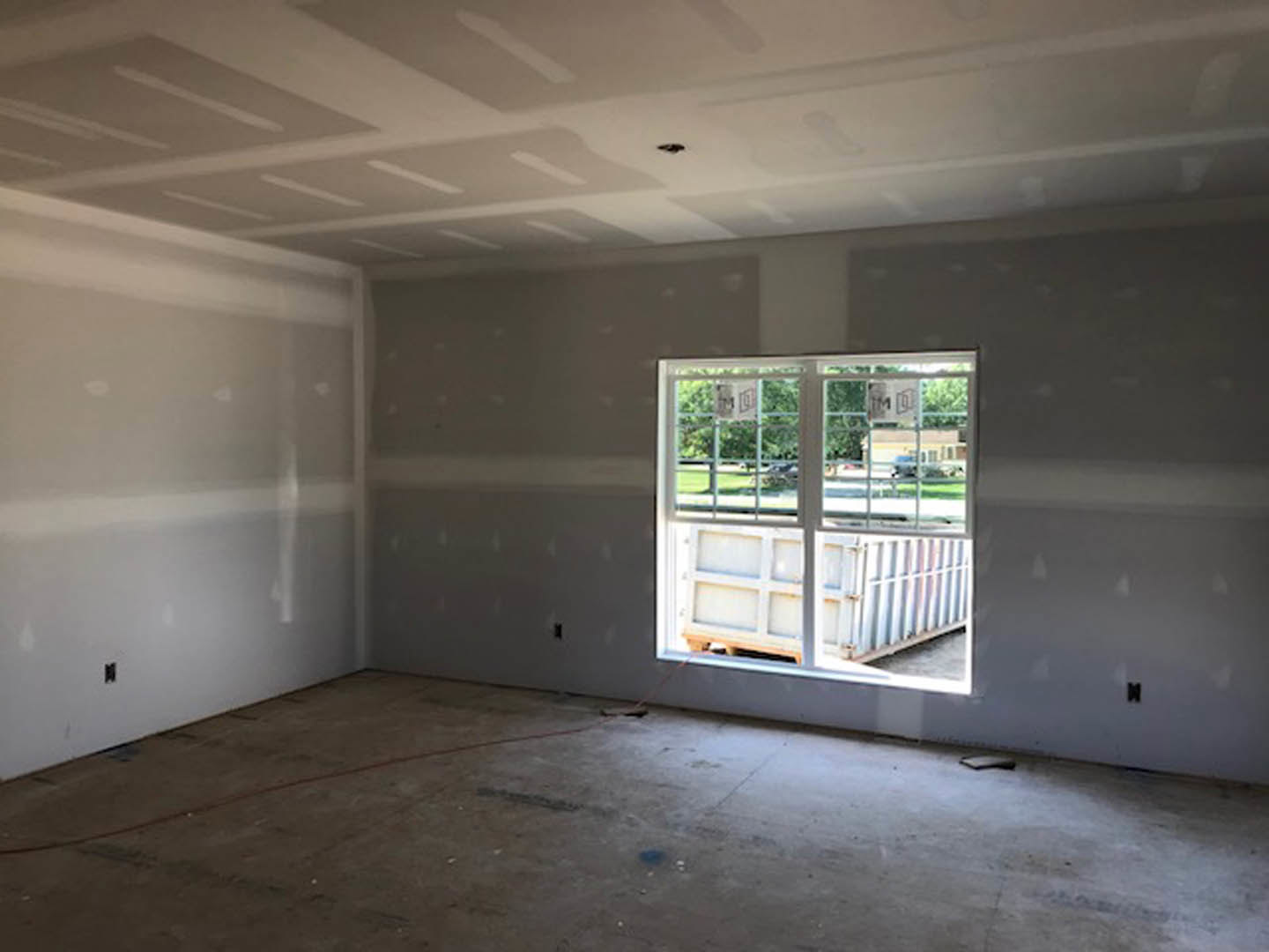 Bright room with two large windows, white plaster walls, light wood floor, ceiling with recessed lighting, red rope tied to one window, outdoor container visible through glass