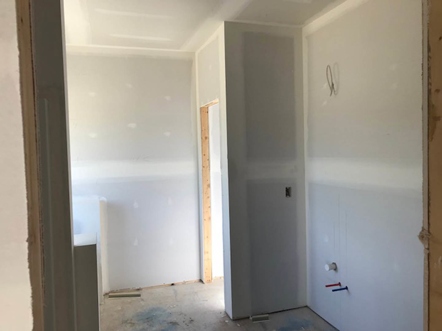 Corner of a room with smooth white plaster walls, white ceiling, light wood flooring, and a white door