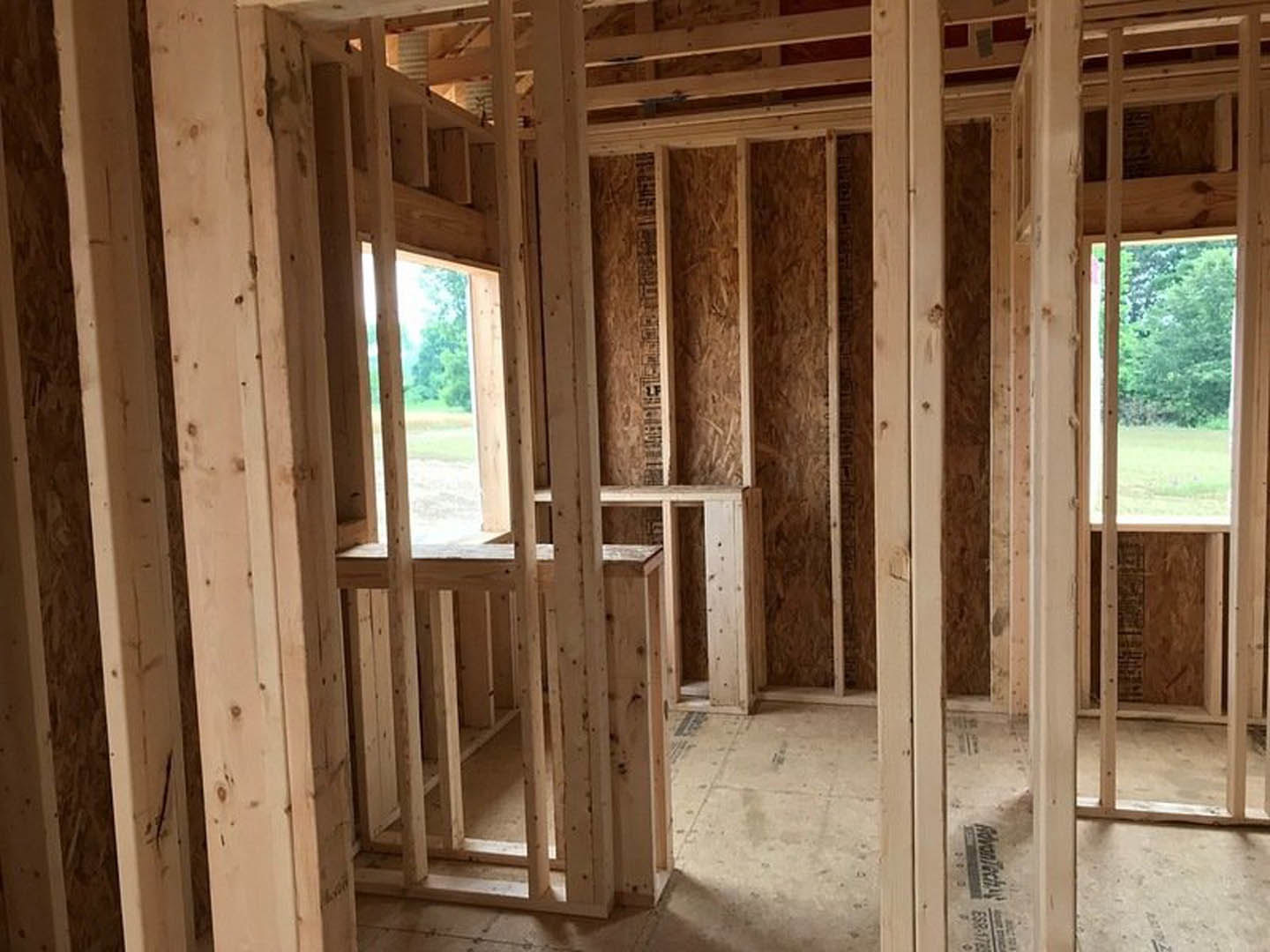 Unfinished room with exposed wood framing, vertical beams, and a window letting in natural light