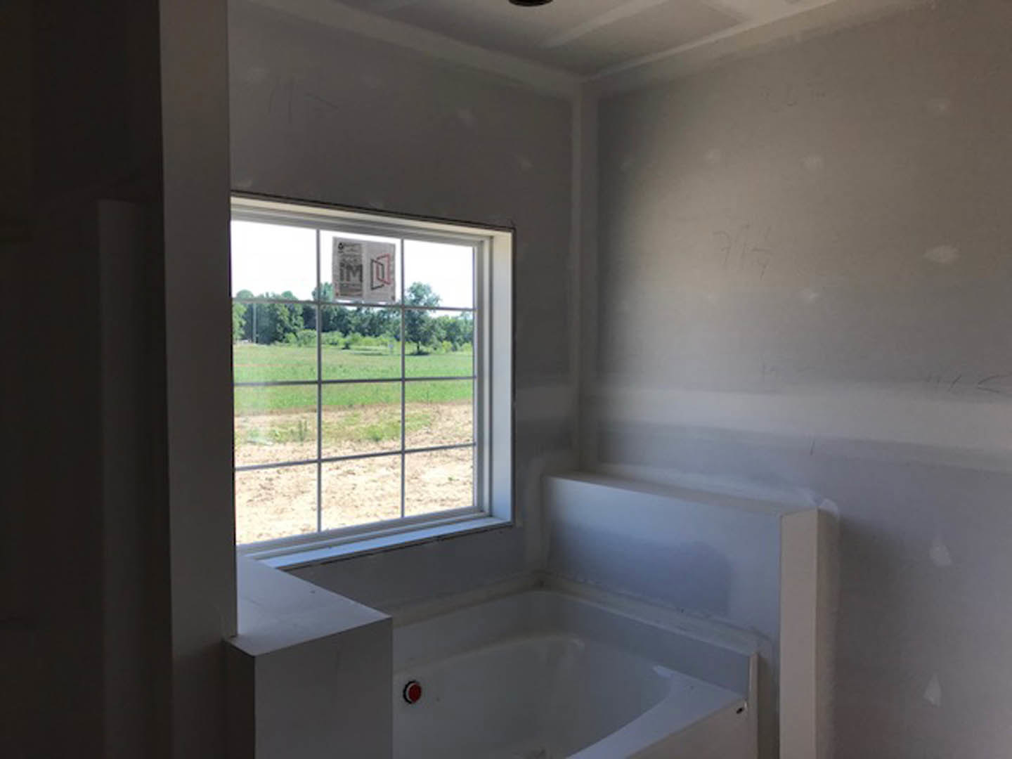 Freestanding white bathtub beneath large window in bright bathroom with light walls and ceiling