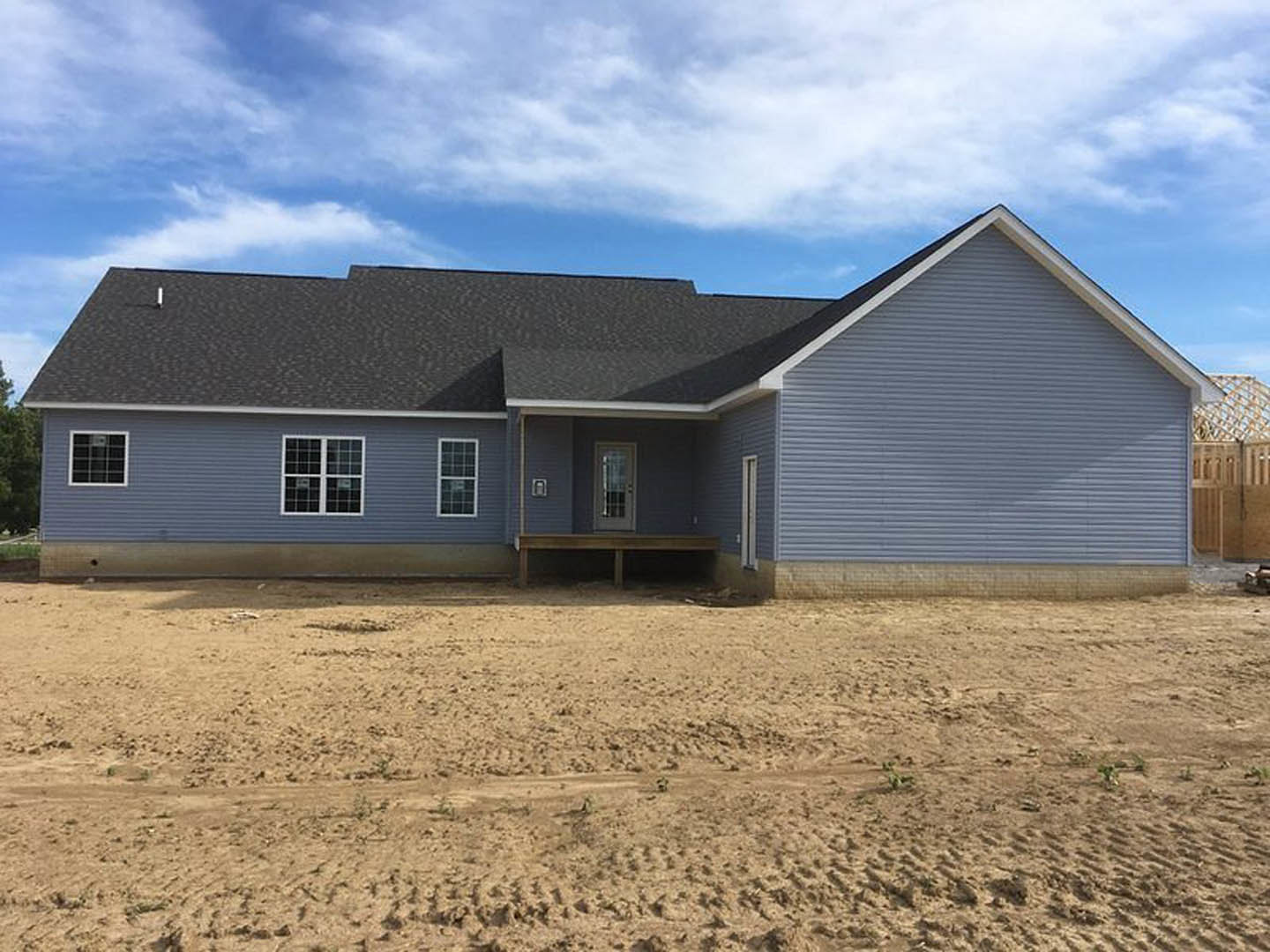 Two-story home with white siding, covered front porch, multi-pane windows, and unfinished dirt yard under cloudy sky