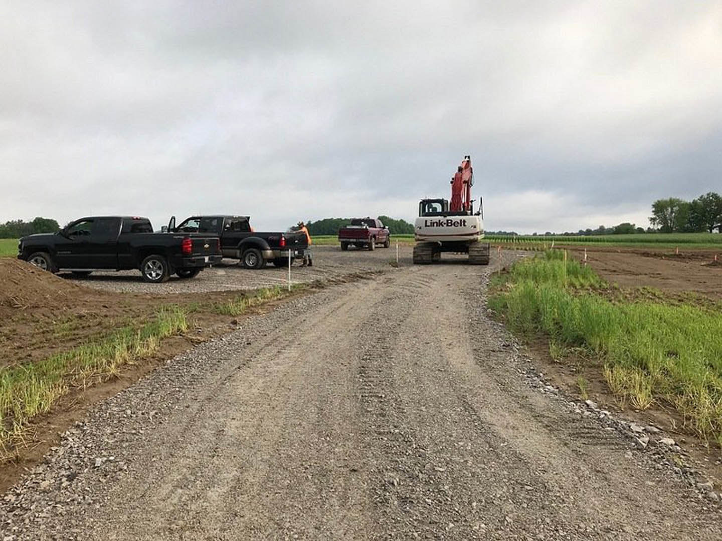 Black pickup truck parked on a dirt road beside grassy field, cloudy sky overhead, man standing in truck bed