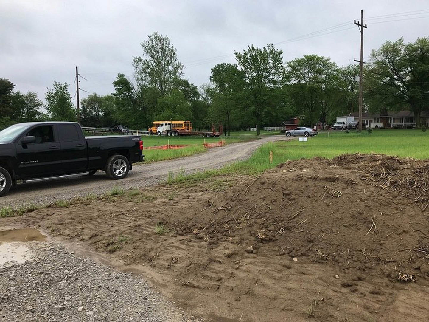 Black pickup truck parked on a dirt road beside grassy terrain, tire tracks visible in soil, trees and sky in background.