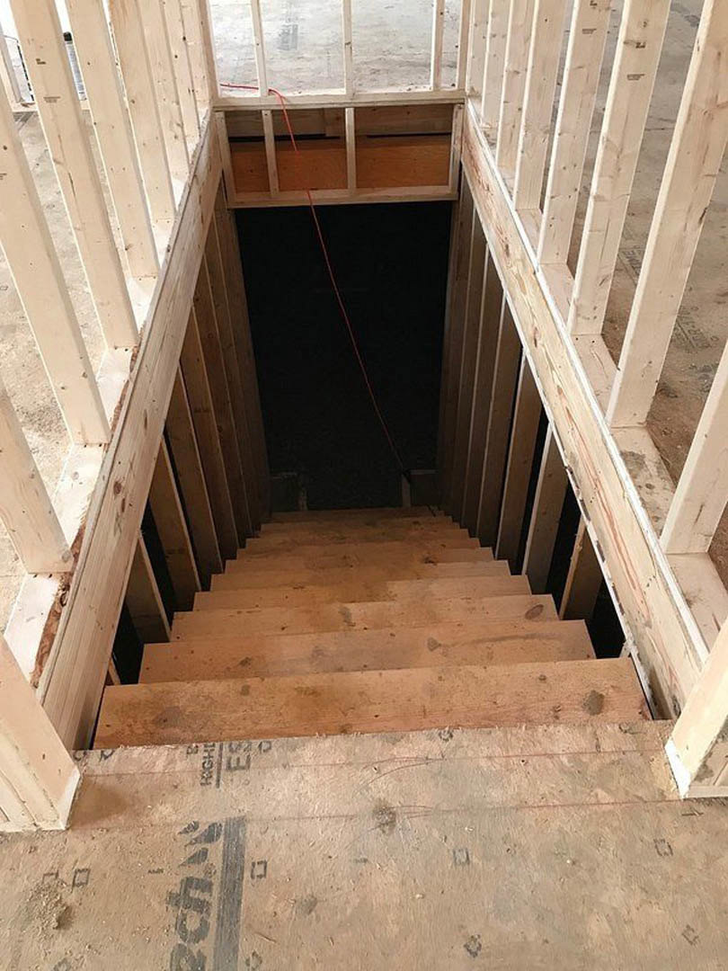 Wooden staircase with metal railing ascending from concrete basement floor, surrounded by dark walls and exposed building materials