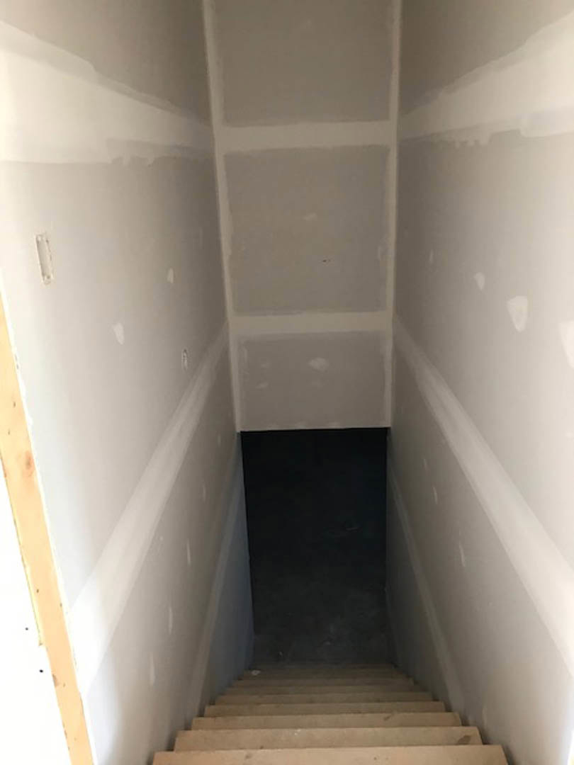Wood staircase with metal railing in a spacious room featuring plaster walls, composite flooring, and a white ceiling