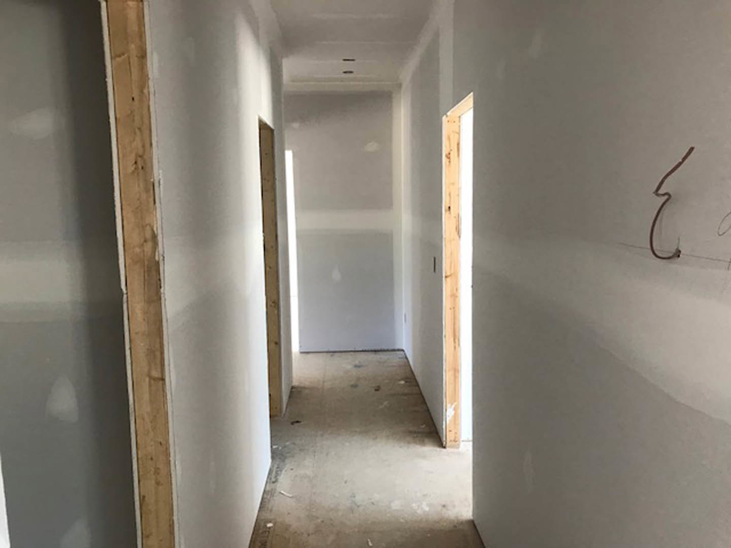 Hallway with smooth white plaster walls, natural wood trim, wooden door, and light-colored flooring