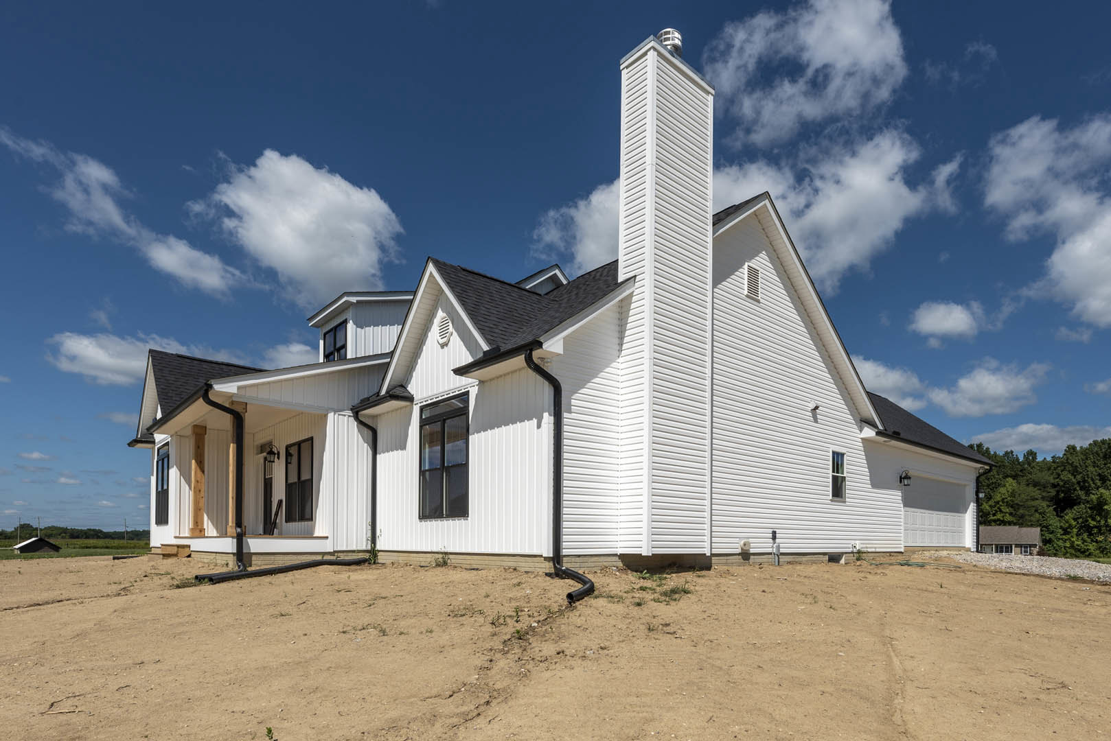 White two-story house with a brick chimney, large windows with white frames, surrounded by trees under a cloudy sky