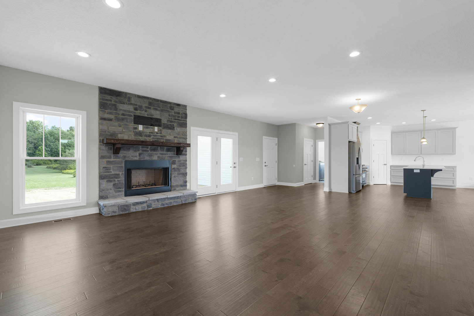 Spacious living room featuring hardwood floors, stone fireplace with curtain, white double doors with glass panels, large window overlooking trees, plaster ceiling and walls