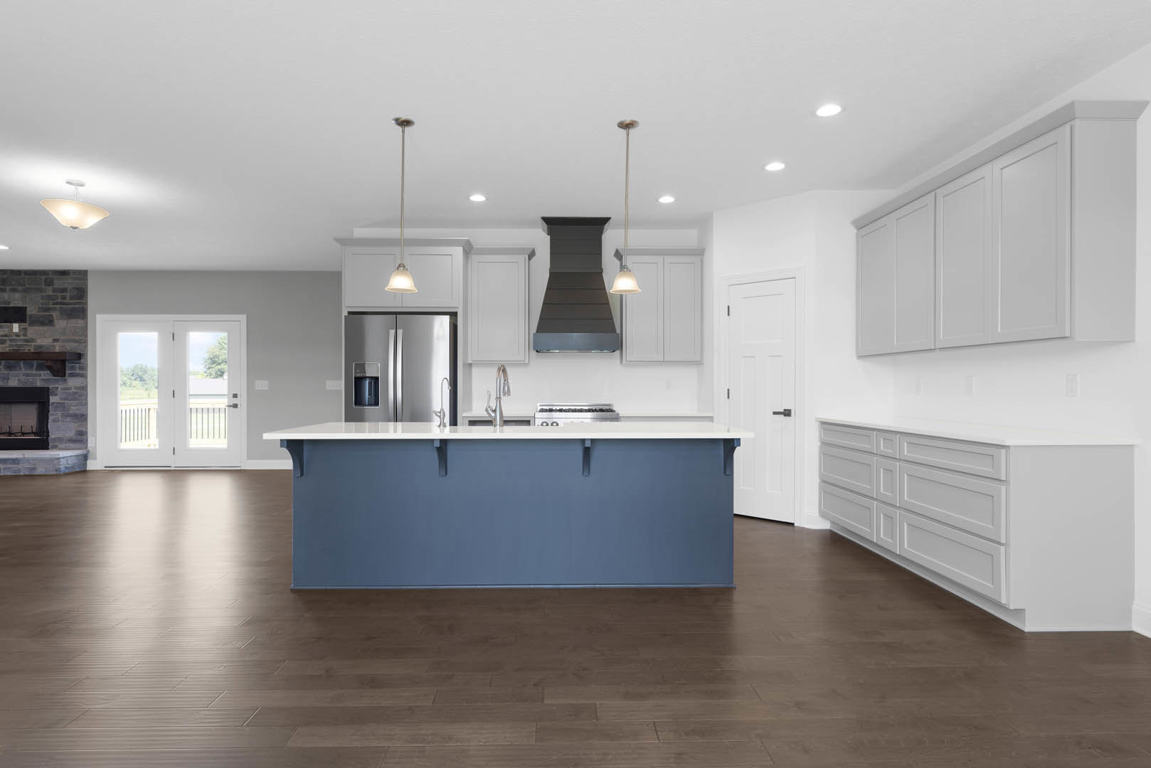 Blue kitchen island with white countertop, stainless steel stove, white cabinetry, glass-paneled double doors, black chair, wooden flooring, and refrigerator.