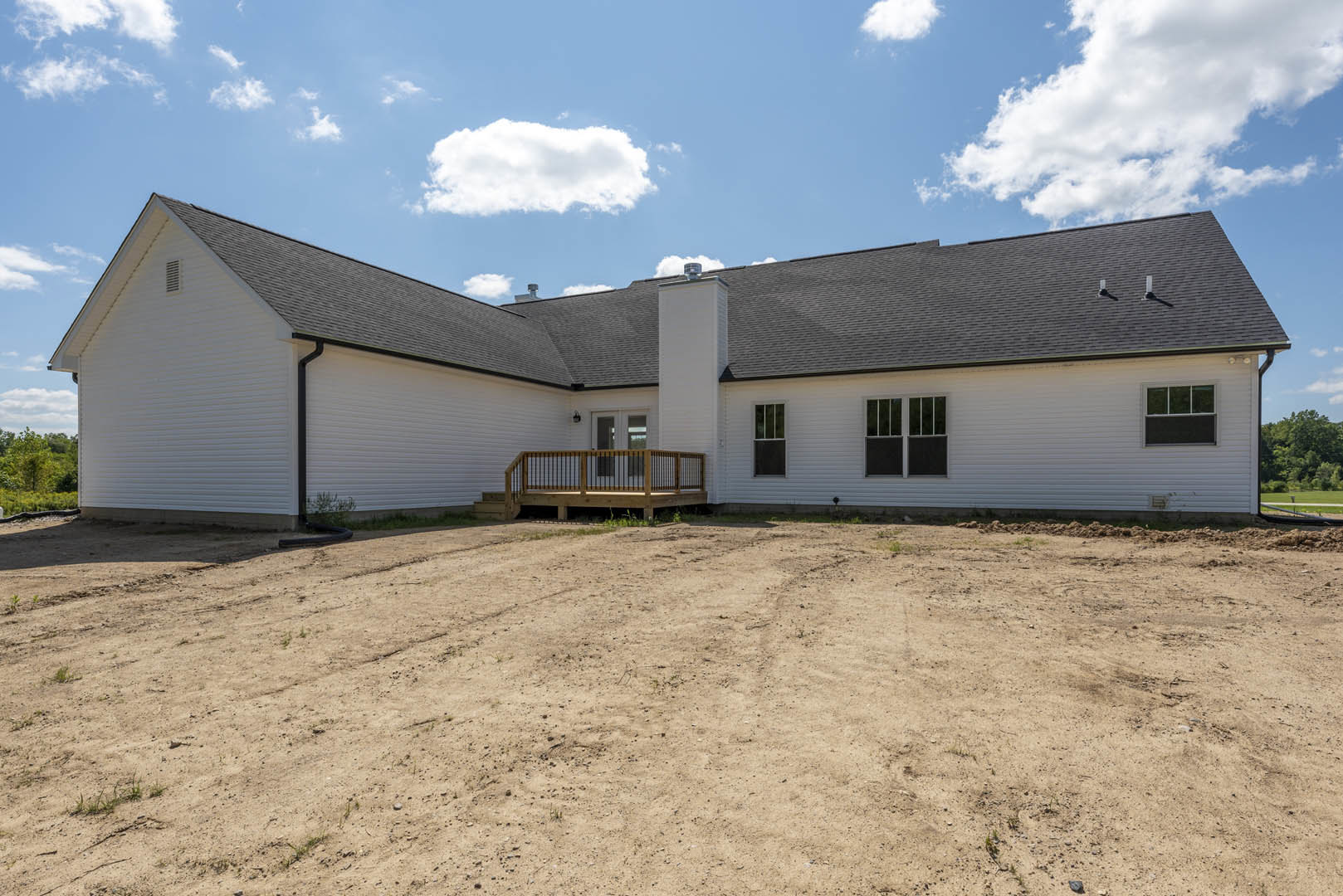 Two-story house with wooden deck and railing, dirt yard in foreground, white-framed windows, cloudy sky above