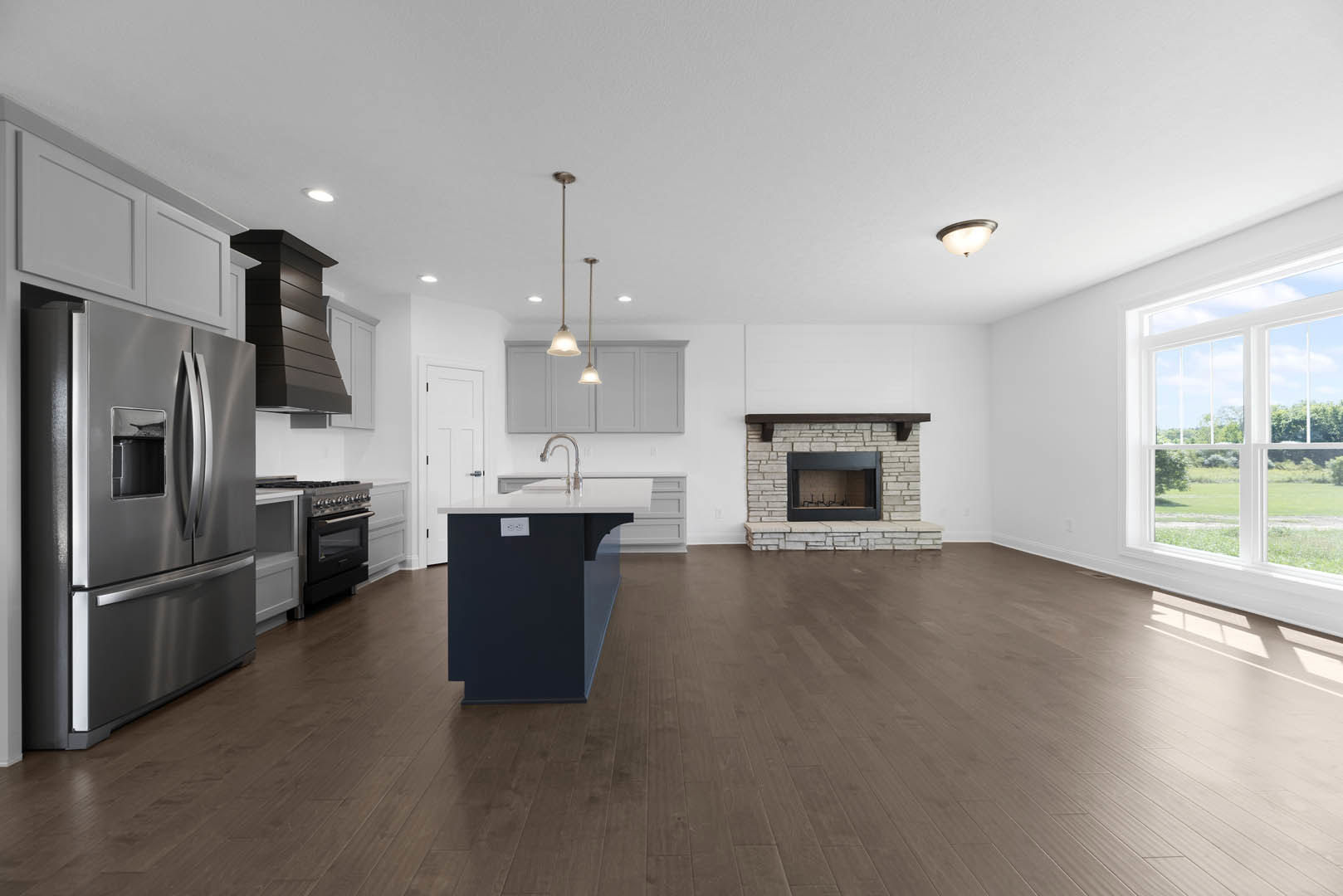 Open-concept kitchen featuring a central island with stone countertop, built-in fireplace with tile surround, stainless steel refrigerator, hardwood flooring, white cabinetry