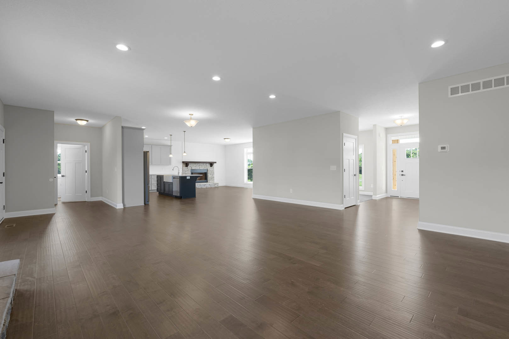 Spacious room with natural wood flooring, white walls, white door featuring glass window and black handles, ceiling light fixture with white shade, partial view of countertop