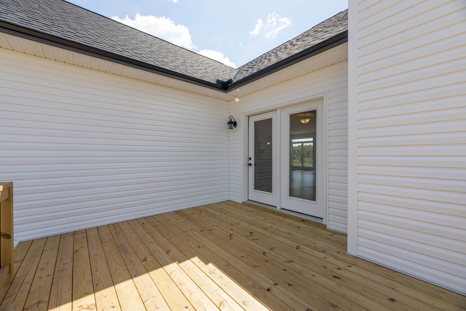 White siding house with wooden deck, glass-paneled door, and large windows reflecting trees.