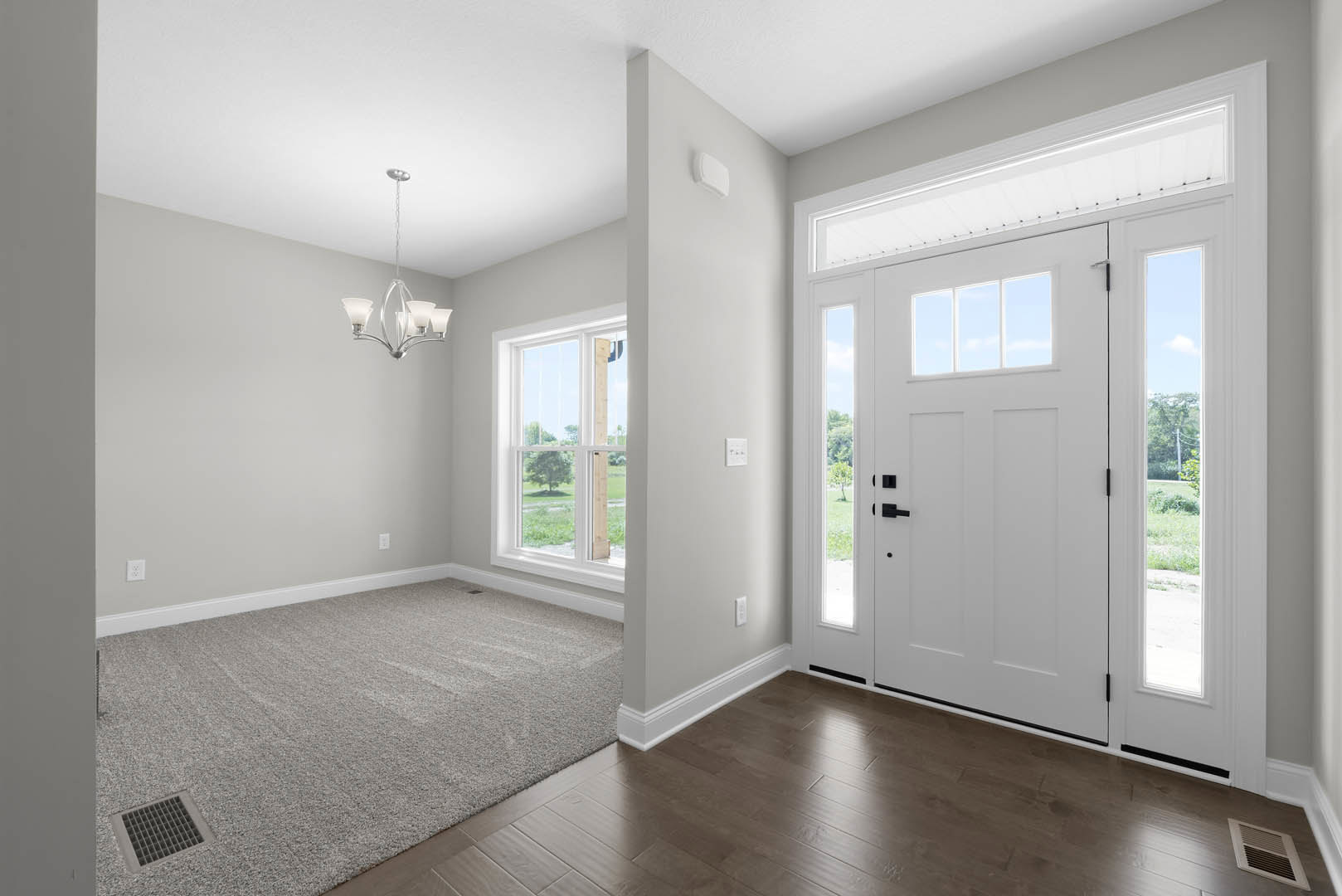 Carpeted room featuring a white door with glass panels, a close-up chandelier, grey wall vent, and window overlooking a leafy tree.