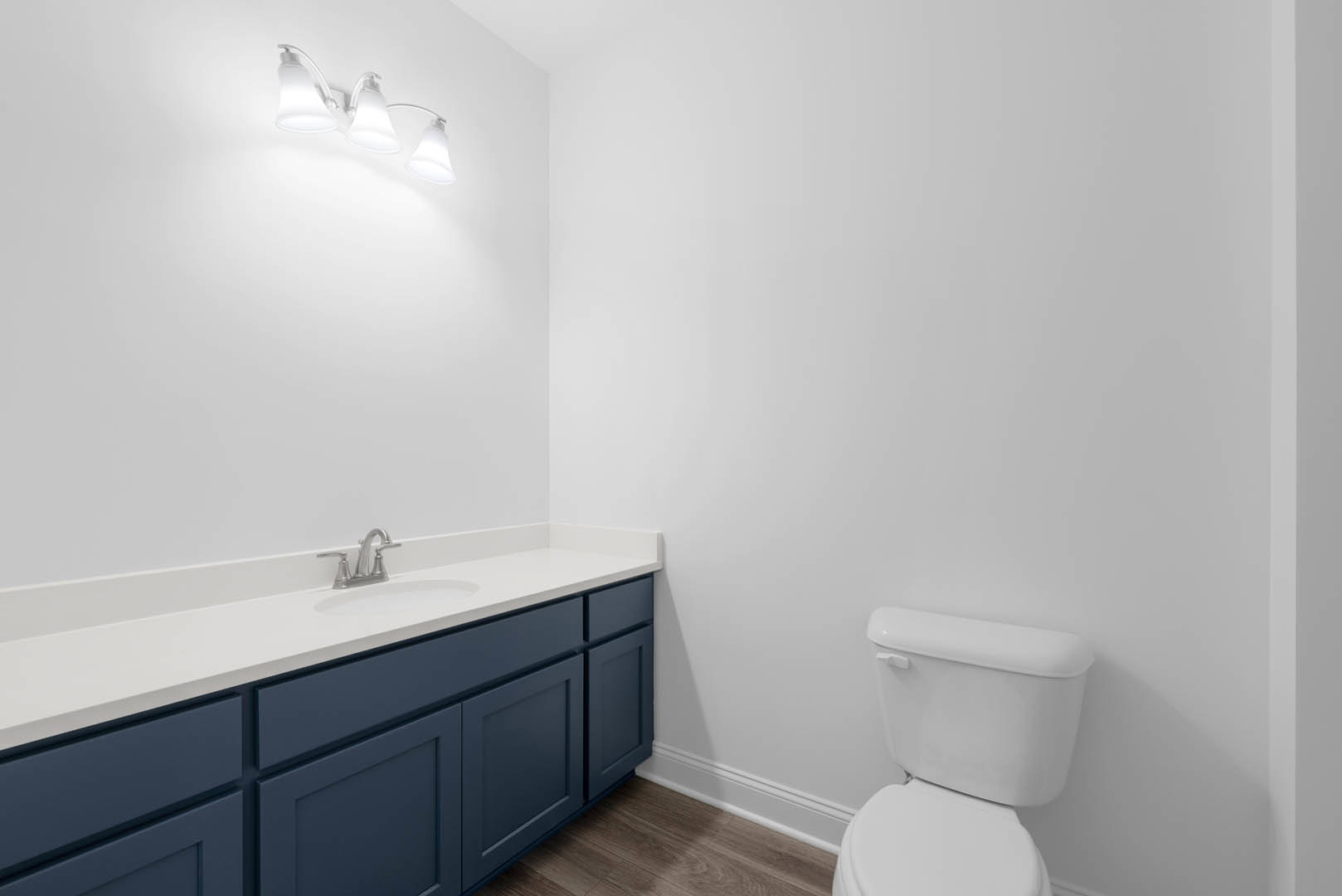 Bathroom with blue shaker cabinets, white countertop, chrome faucet, toilet, and tiled walls