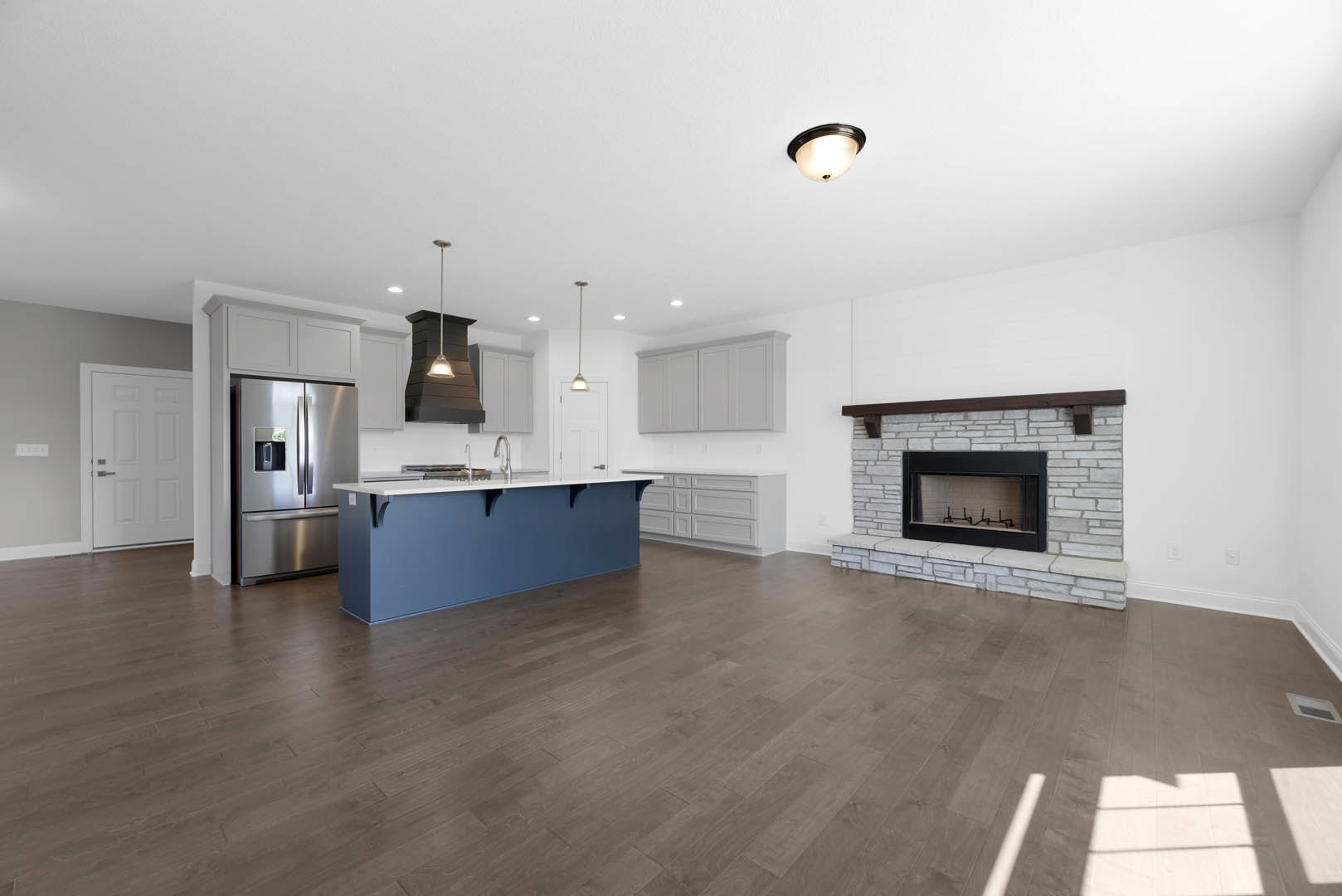 Open-concept kitchen and living room featuring a black-framed fireplace, blue island with white countertop, stainless steel refrigerator, wood and laminate flooring, modern ceiling