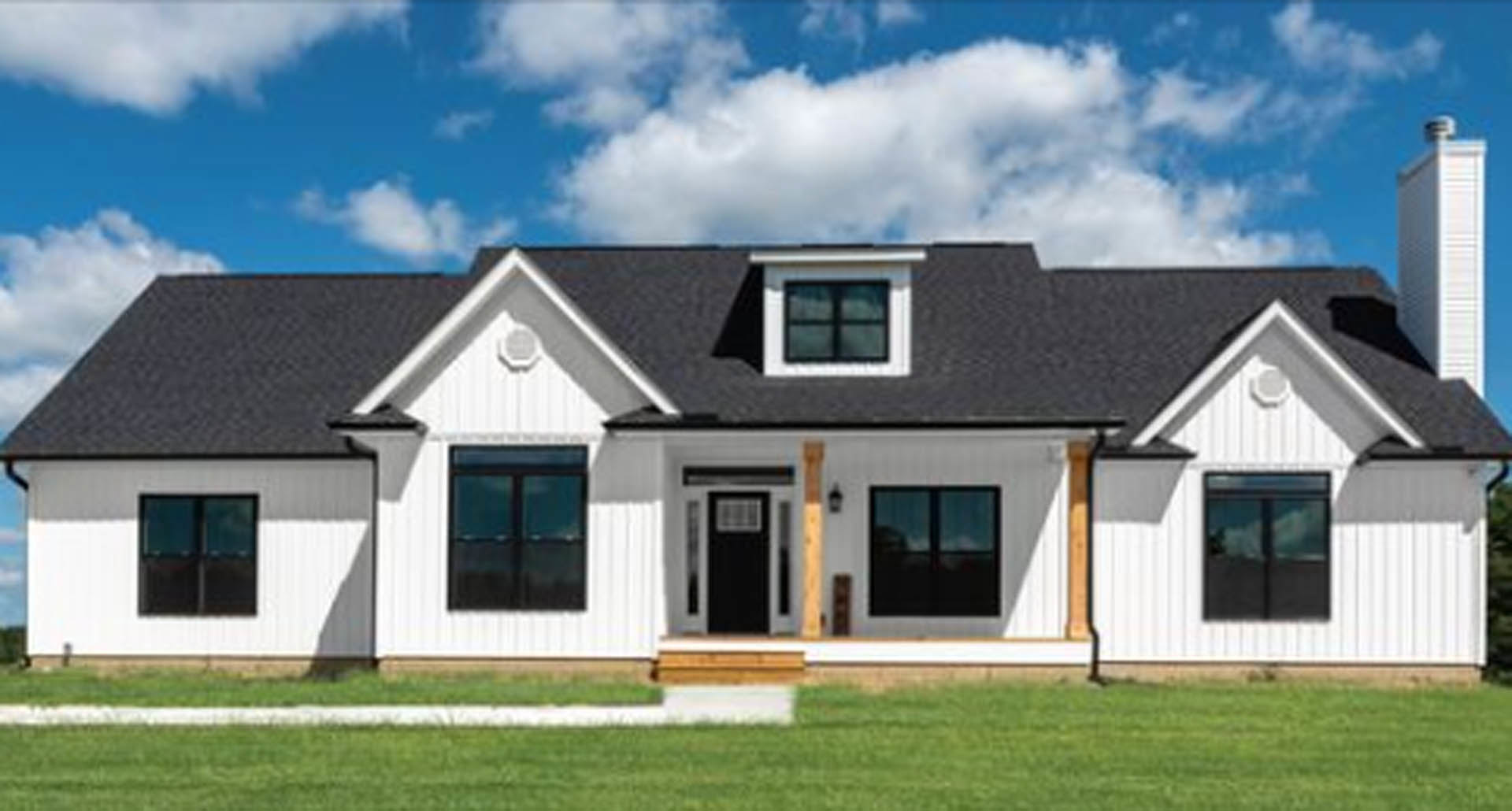 White siding home with black framed windows, black and white front door, covered porch, green lawn, and partly cloudy sky.