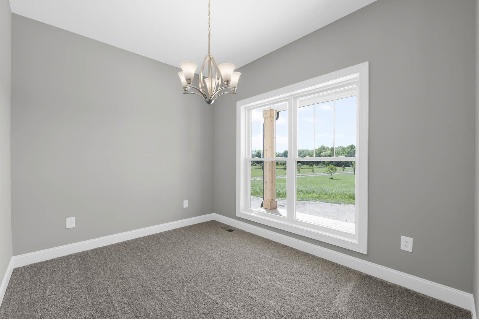 Carpeted room with a large window, white electrical outlet on the wall, wooden trim framing the window, close-up of a chandelier, and white molding along a wooden accent wall
