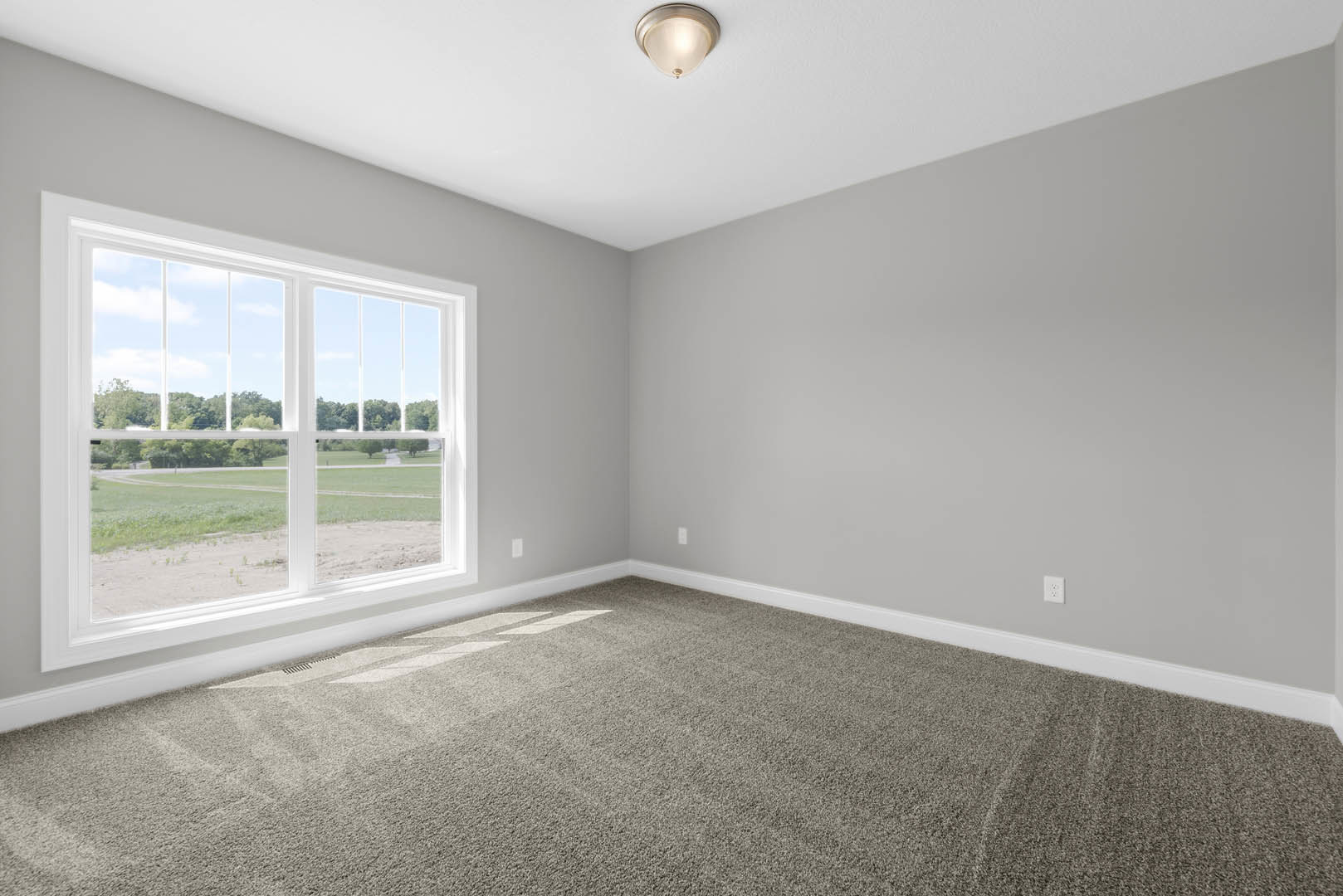 Carpeted room with white walls, ceiling light fixture, large window overlooking grassy field and trees