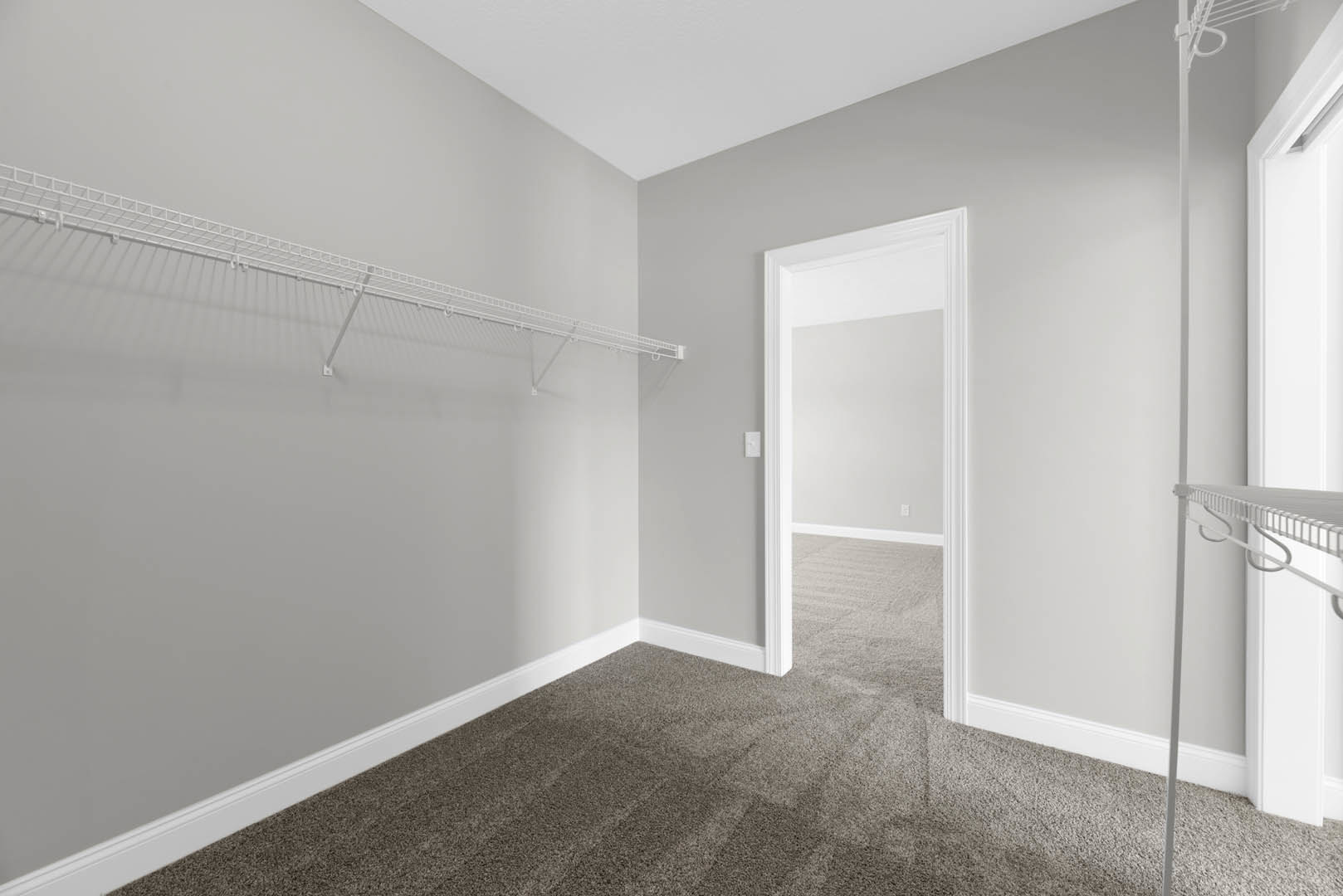 White built-in shelf with hooks mounted on a white wall, beige carpet flooring, and a white door in a bright interior room.