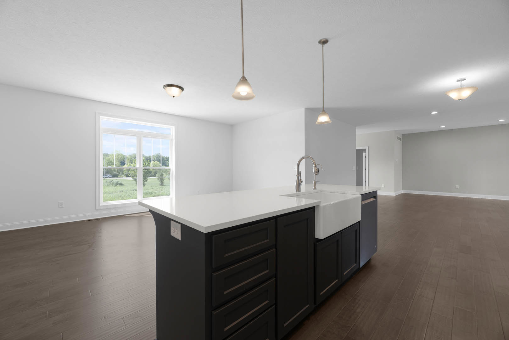 Spacious kitchen featuring a large central island with white countertop, built-in sink and drawers, wide window overlooking green lawn, modern cabinetry, and ceiling light fixture