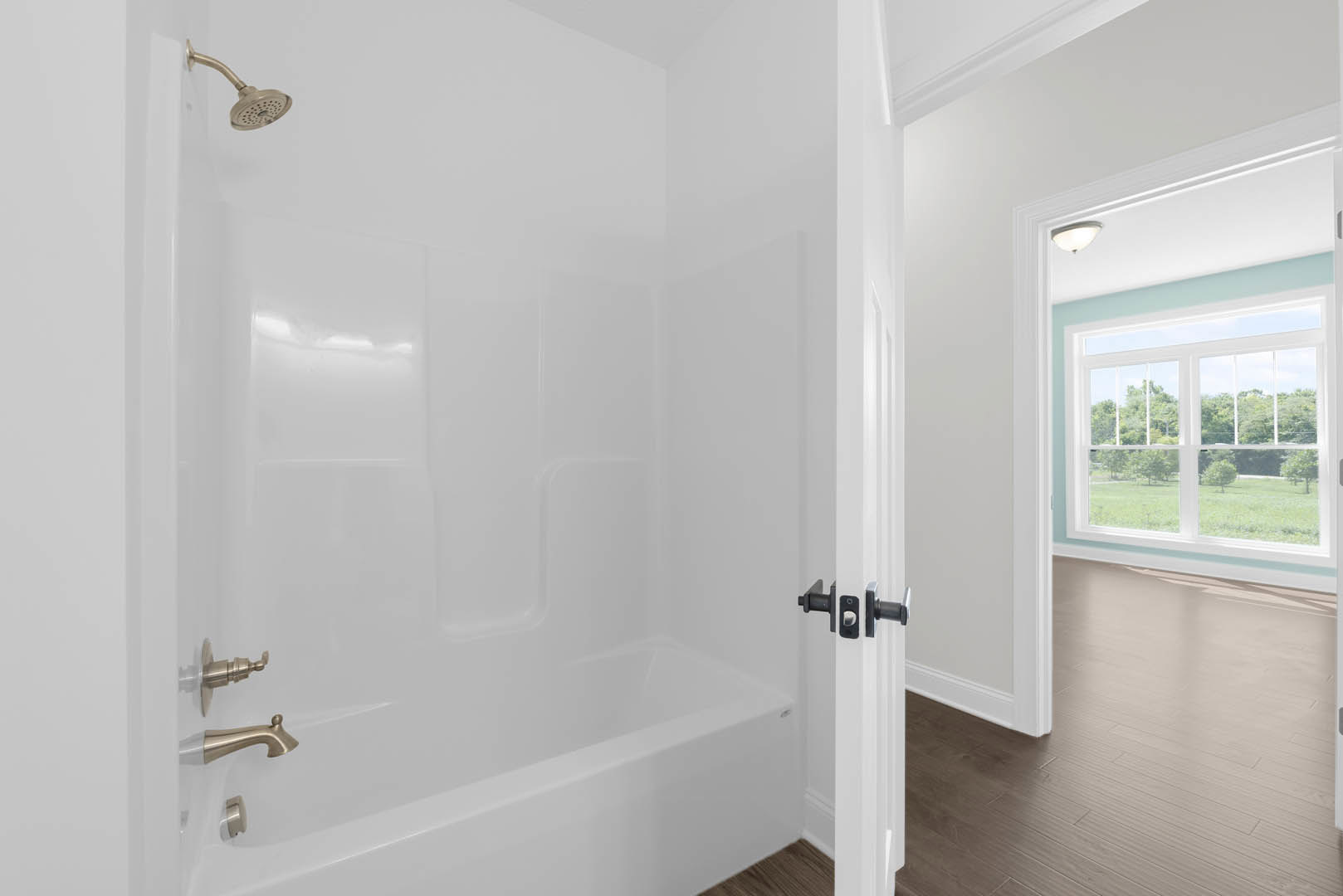 White-tiled bathroom featuring a glass-enclosed shower, freestanding soaking tub, chrome faucet, and large window overlooking leafy trees