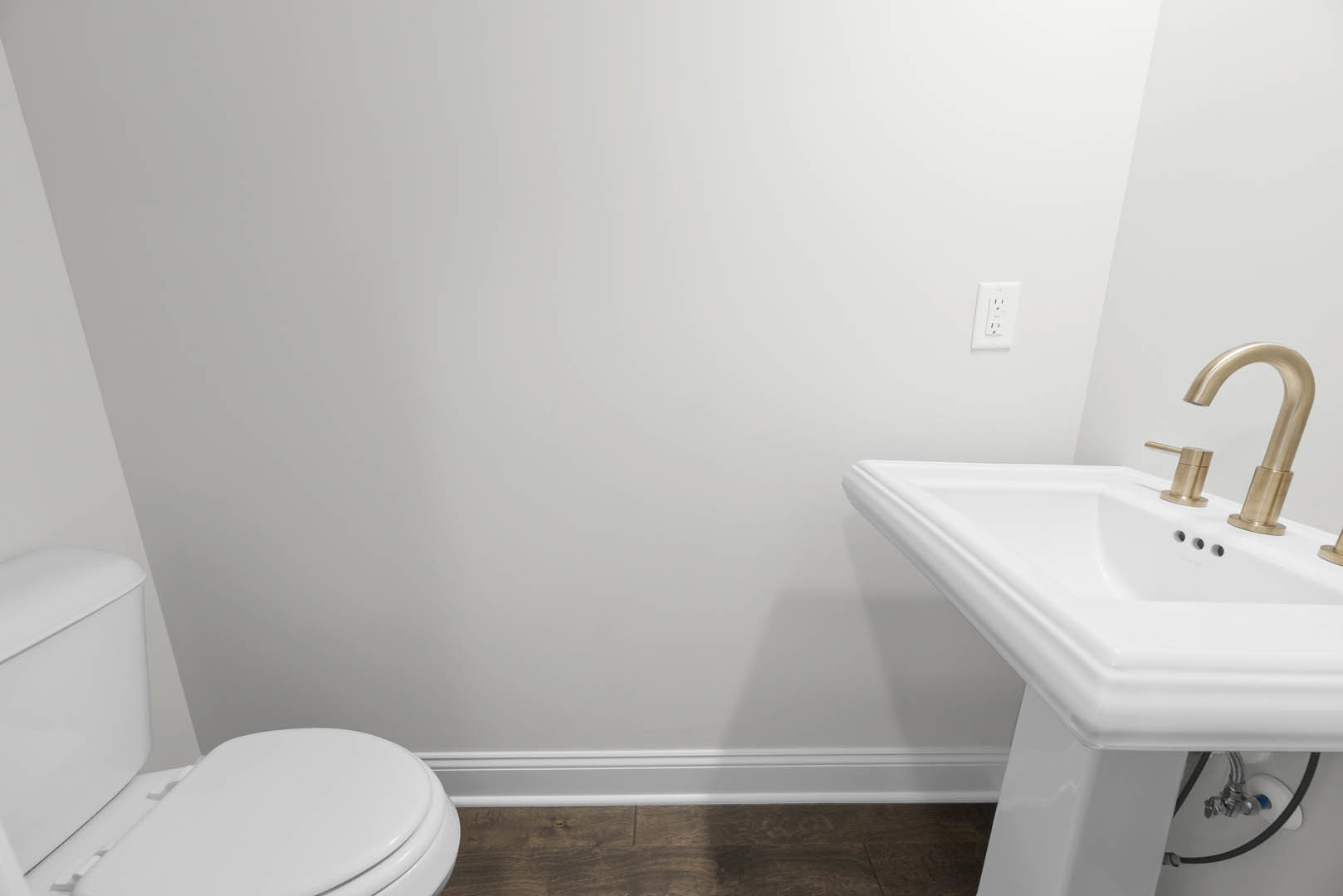 White bathroom featuring a porcelain sink with gold faucets, a close-up of a modern toilet, white tile walls, a wood countertop, and a white outlet with black buttons.