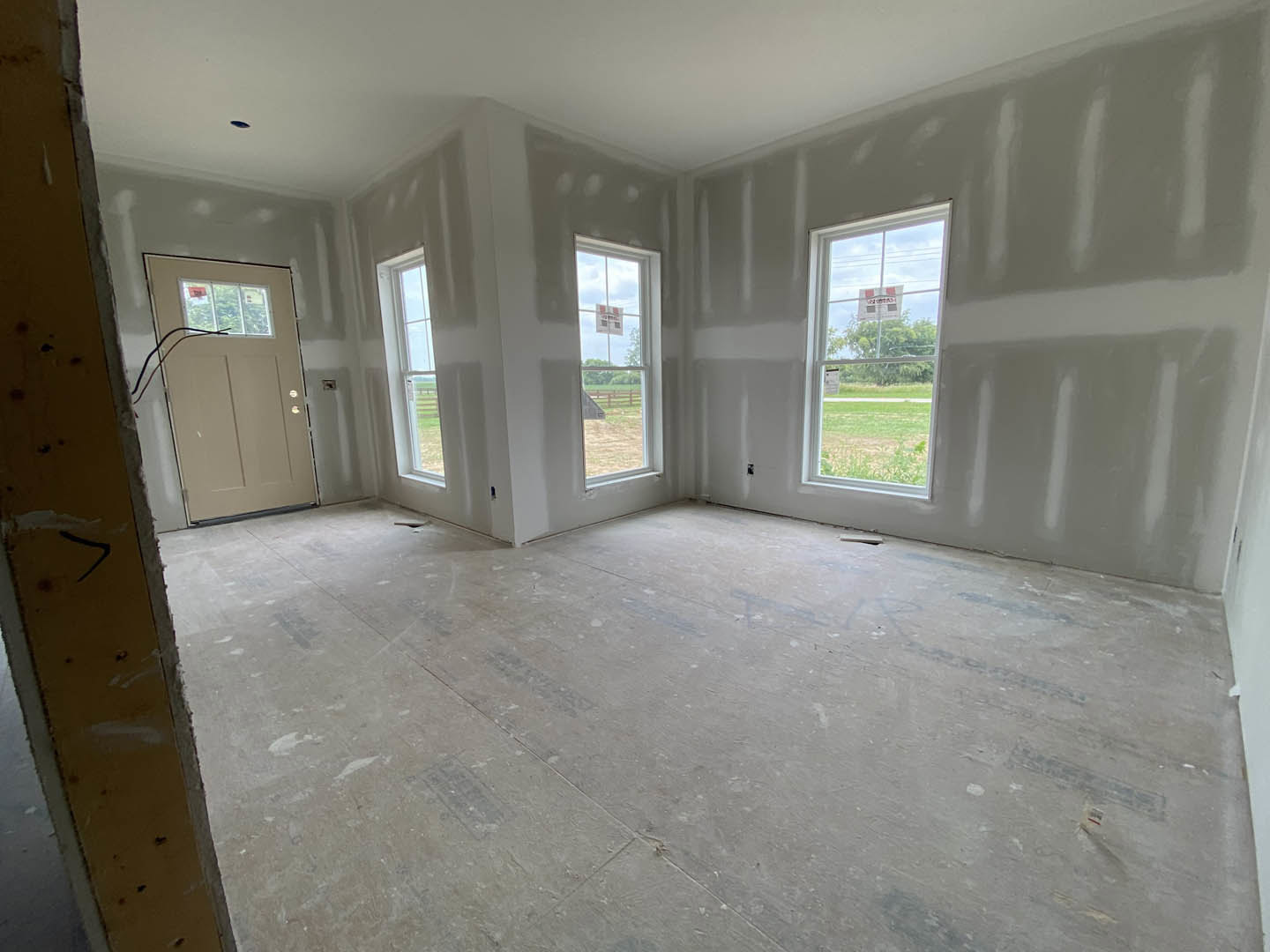 White-walled room with large windows, wood flooring, and a single door; natural light streams in through glass panes.