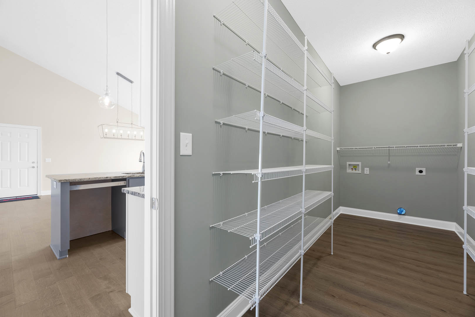 Built-in white shelves along one wall, light wood flooring, white cabinetry with silver handles, quartz countertop with undermount sink, recessed ceiling light fixture.