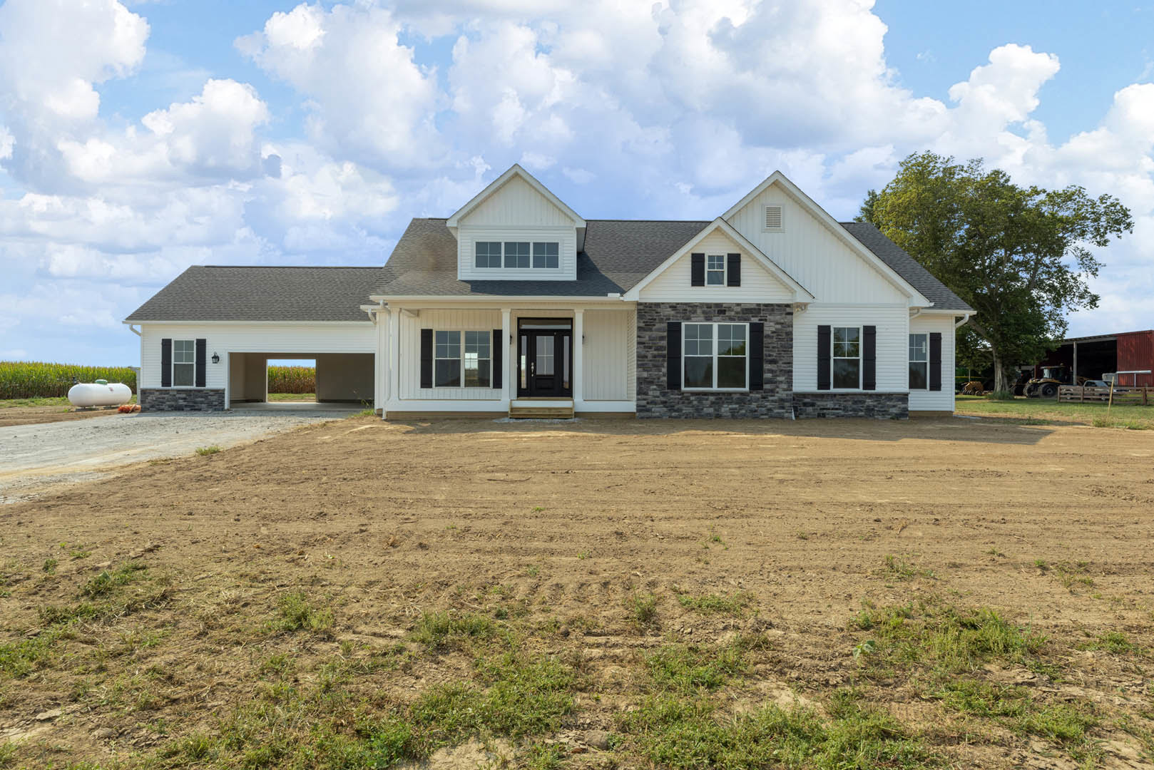 Two-story white house with black front door, stone accent wall, large paved driveway, white-framed windows, manicured grass, and blue sky overhead