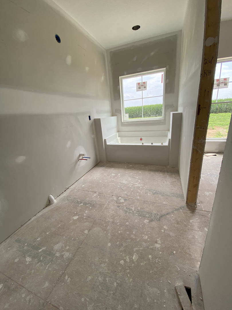 Bathroom with freestanding tub beneath a window, plaster walls, light-colored flooring, and ceiling fixture.