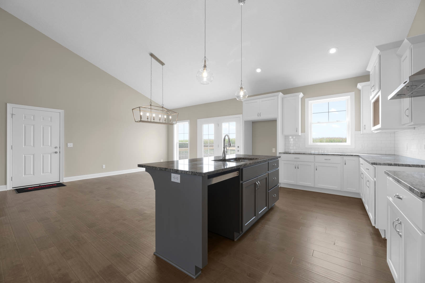 Open kitchen with wood flooring, white cabinetry, marble-topped island featuring an undermount sink, stainless steel hardware, large window overlooking grassy field, slim black