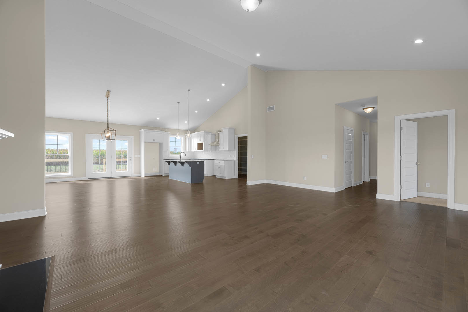 Spacious open floor plan featuring wood flooring, kitchen with grey and white countertops, dining area, white walls, structural pole, and white double doors with glass panes.