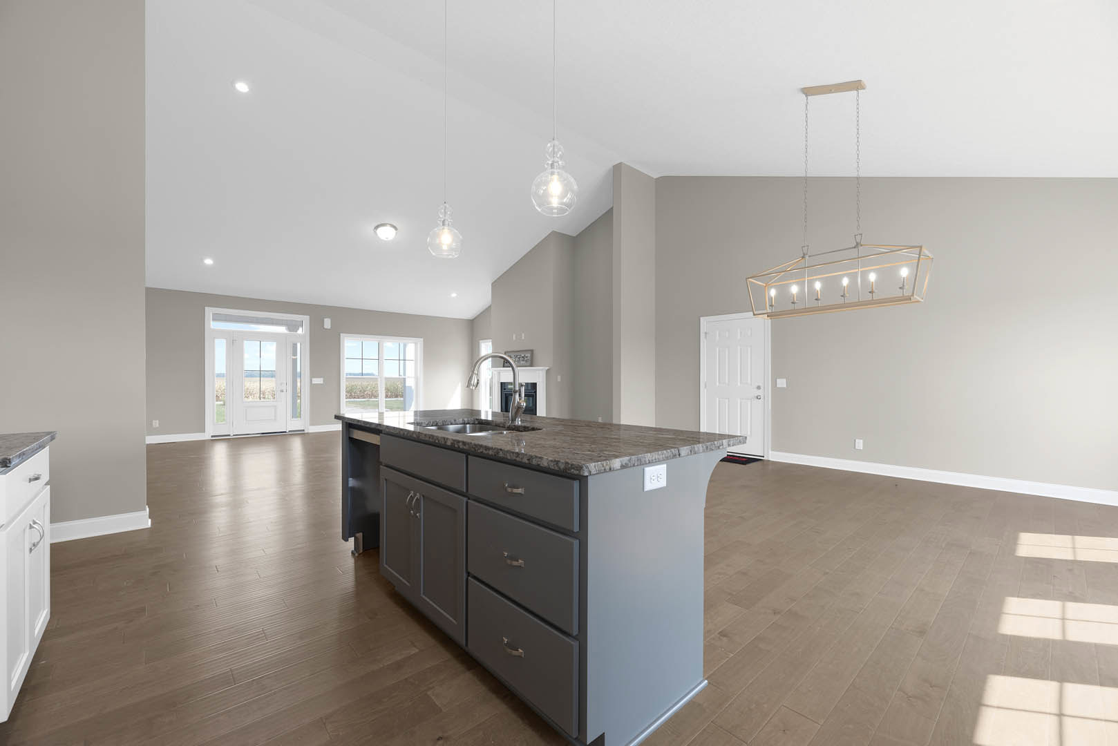 Open-concept kitchen and living room featuring a large island with built-in sink, white cabinetry, wood flooring, candle-style ceiling light fixture, and a white door with glass